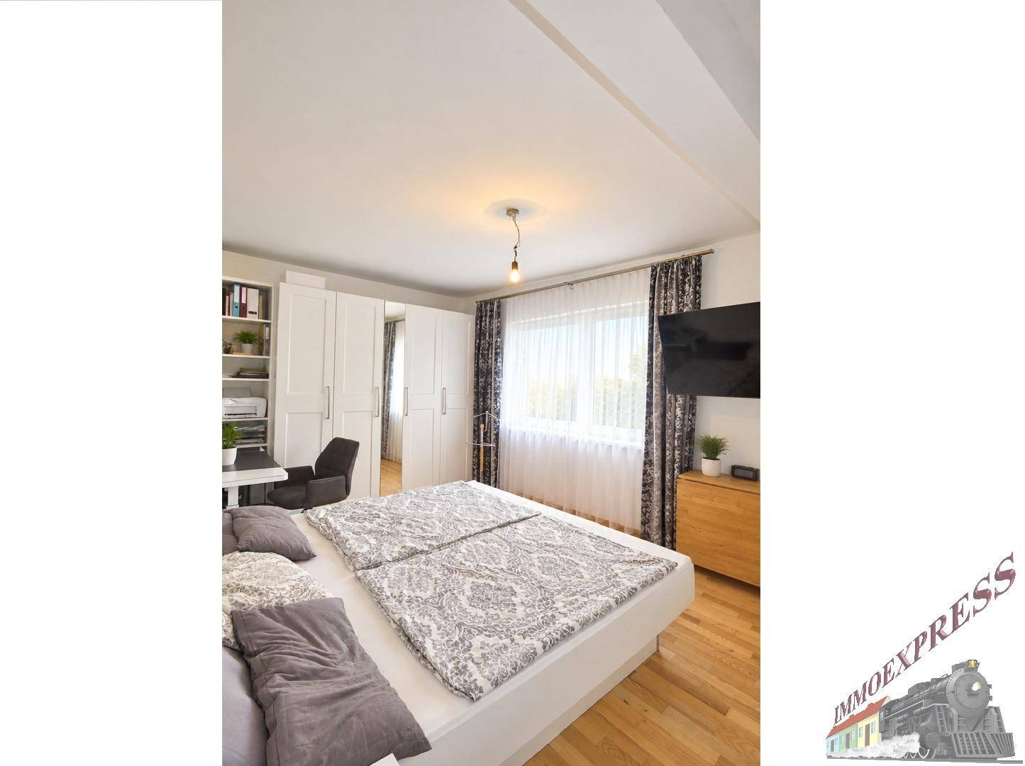 Helles Schlafzimmer mit großem Fenster, Doppelbett und integriertem Arbeitsbereich.