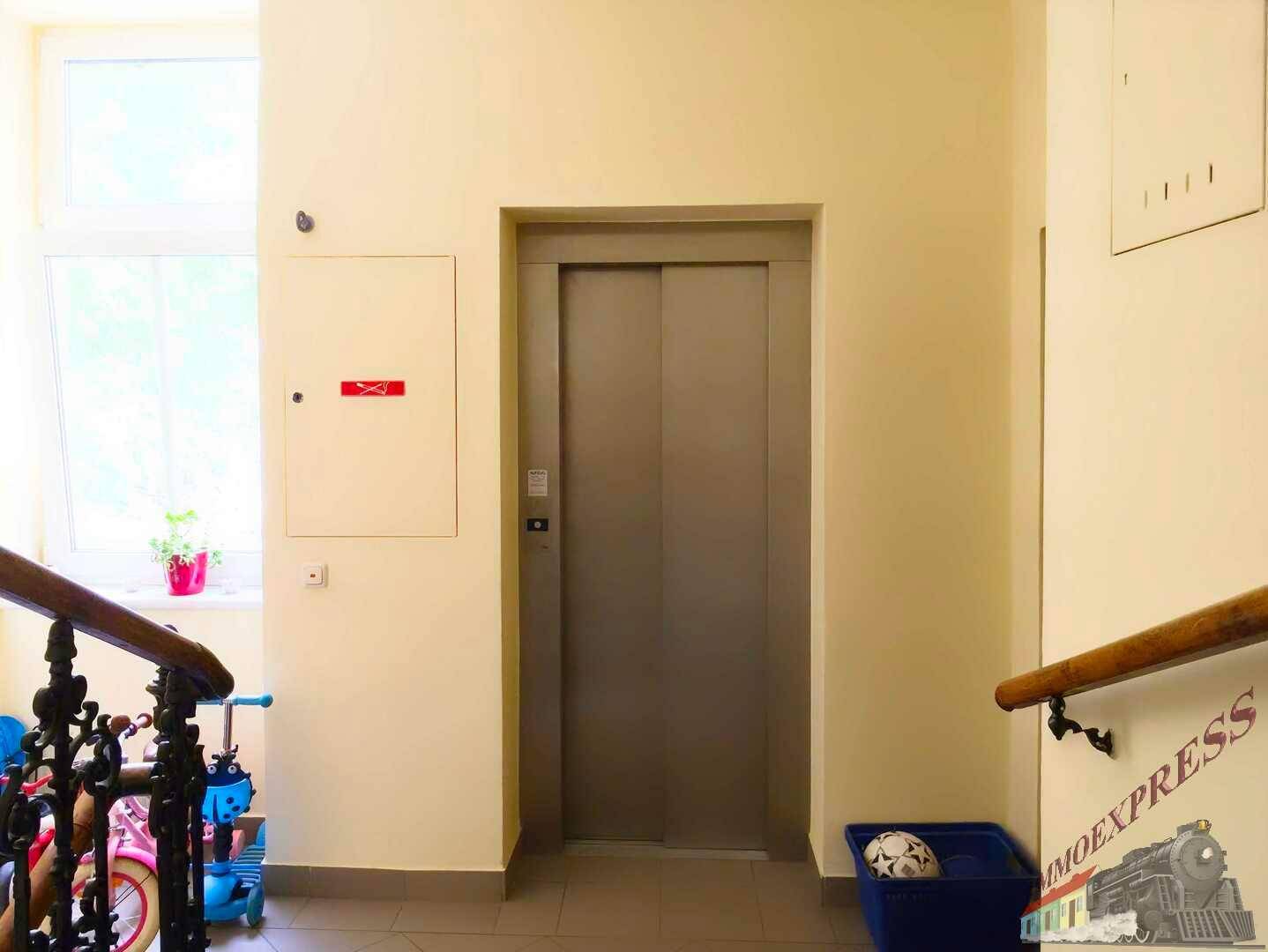 Heller Flur mit Aufzug, Fenster und einem Bereich für Kinderfahrzeuge.