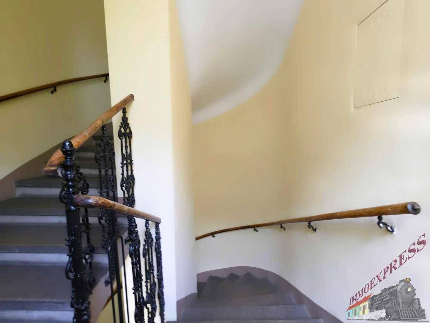 Geschwungene Treppe mit Holzgeländer und schmiedeeisernen Details in einem Treppenhaus.