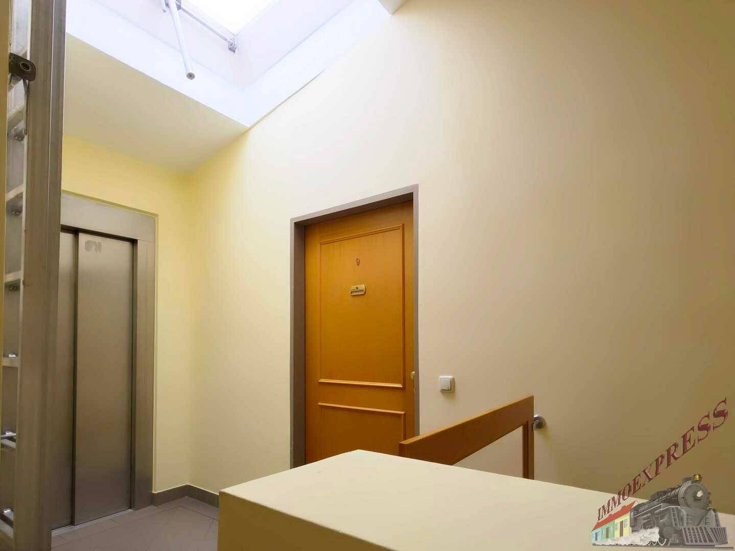 Heller Flur mit Aufzug, Wohnungstür und Oberlicht, das für natürliches Licht sorgt.