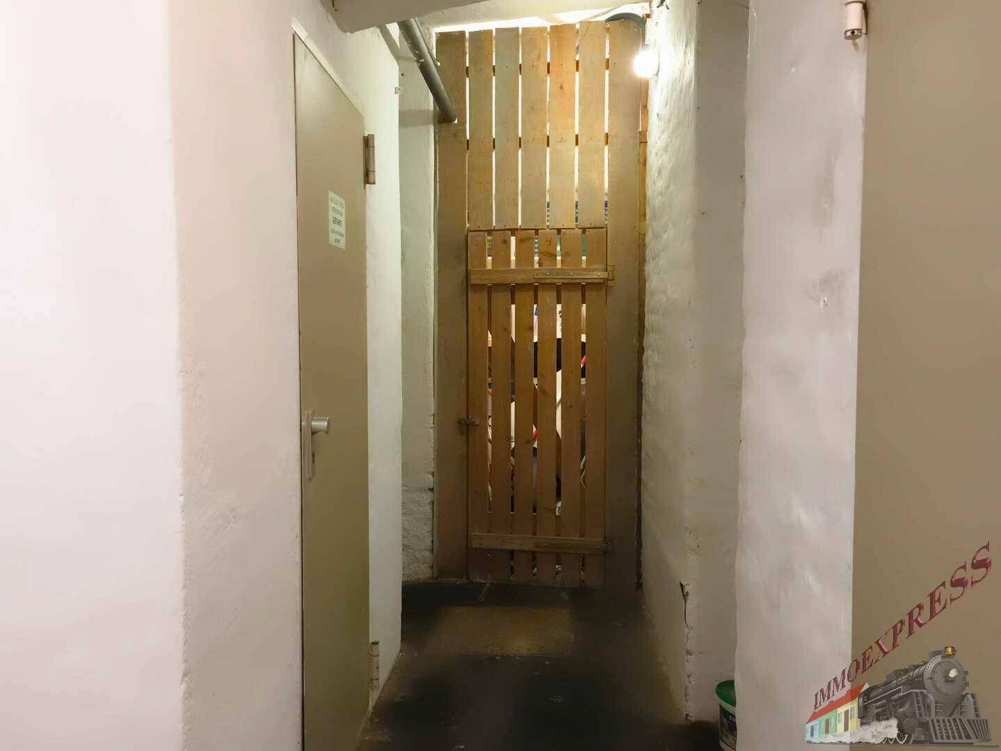 Schmaler Kellergang mit Holztüren und einfachen Wänden, der zu Abstellräumen führt.