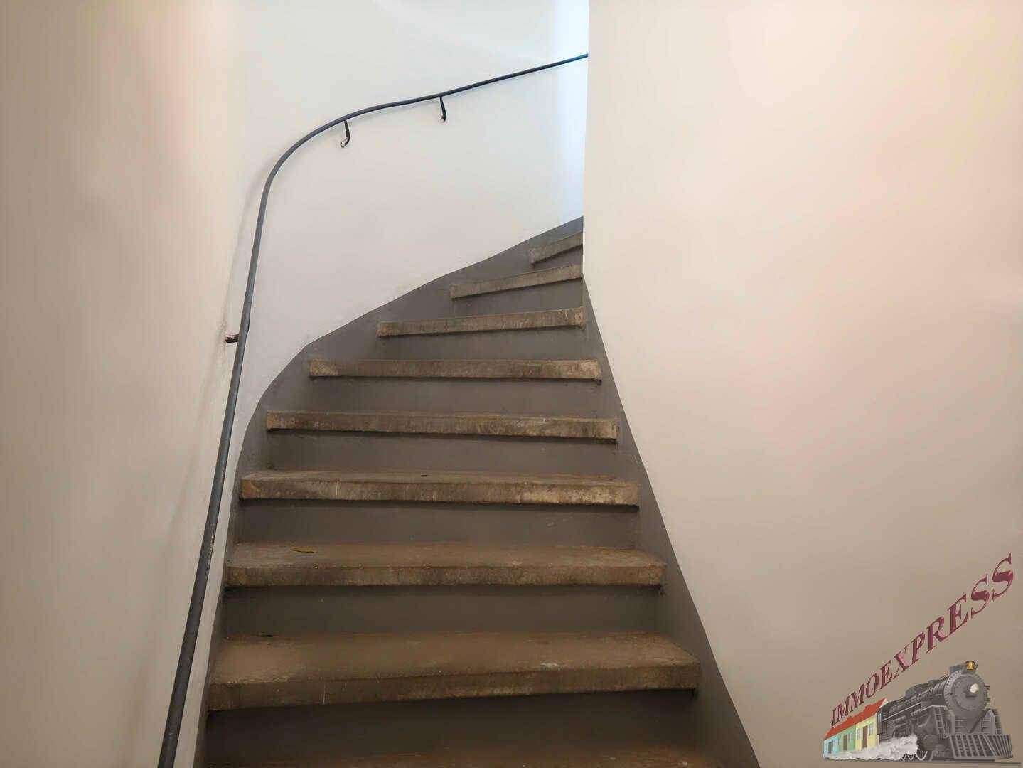 Wendeltreppe mit Steinstufen und einem einfachen Metallgeländer in einem Treppenhaus.