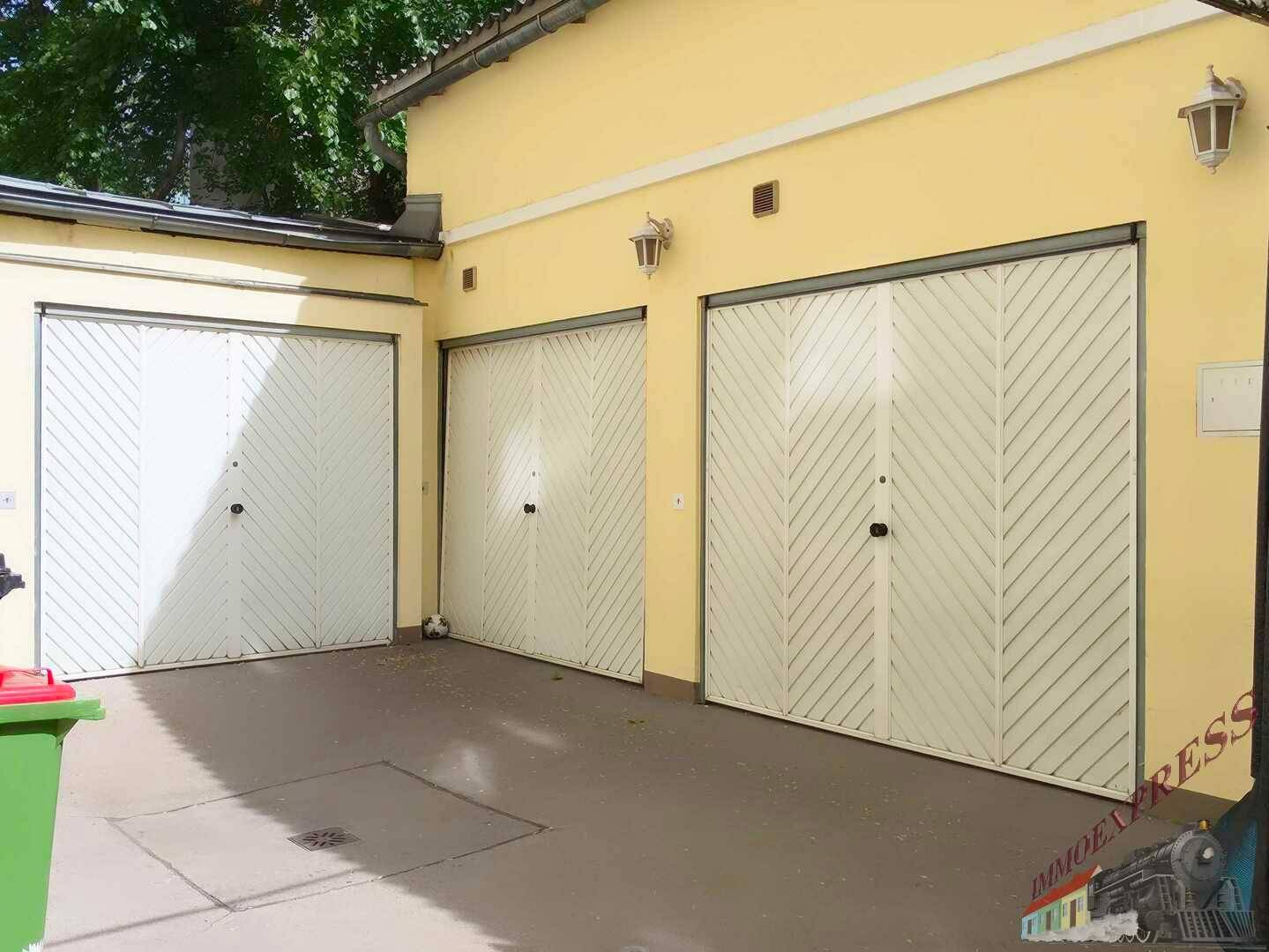 Drei Garagentore an einem gelben Gebäude mit einem gepflasterten Vorplatz.