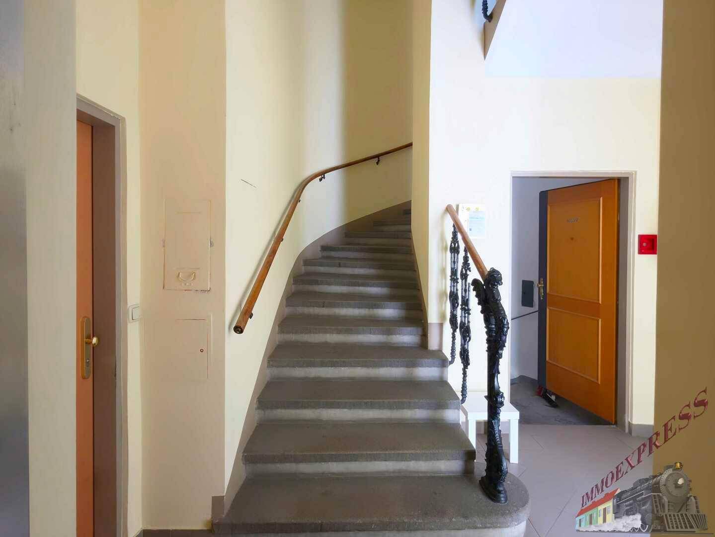 Geschwungene Treppe mit Steinstufen und einem verzierten Geländer in einem Mehrfamilienhaus.