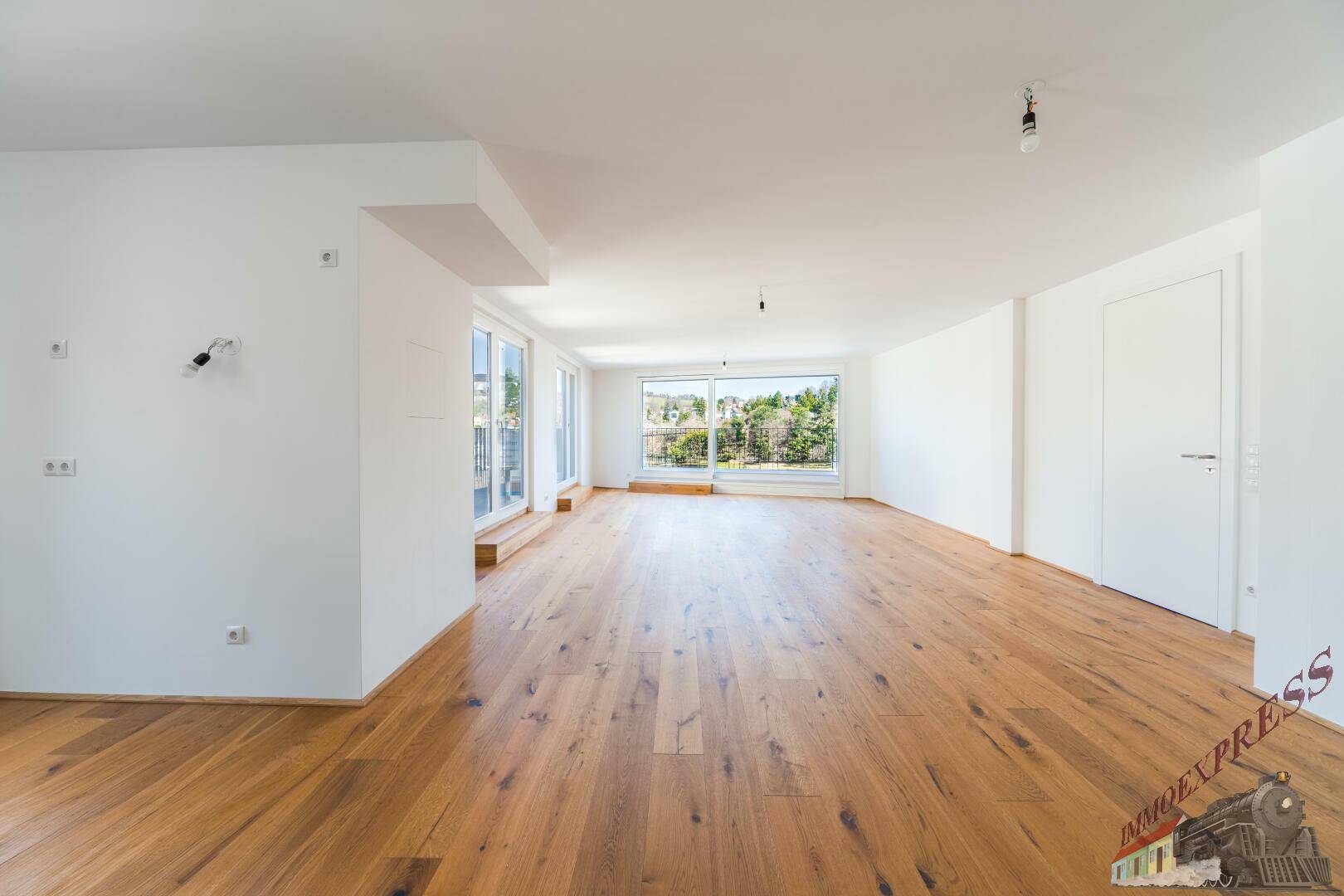 Geräumiges, lichtdurchflutetes Wohnzimmer mit hellem Holzfußboden und Zugang zu Außenbereichen.