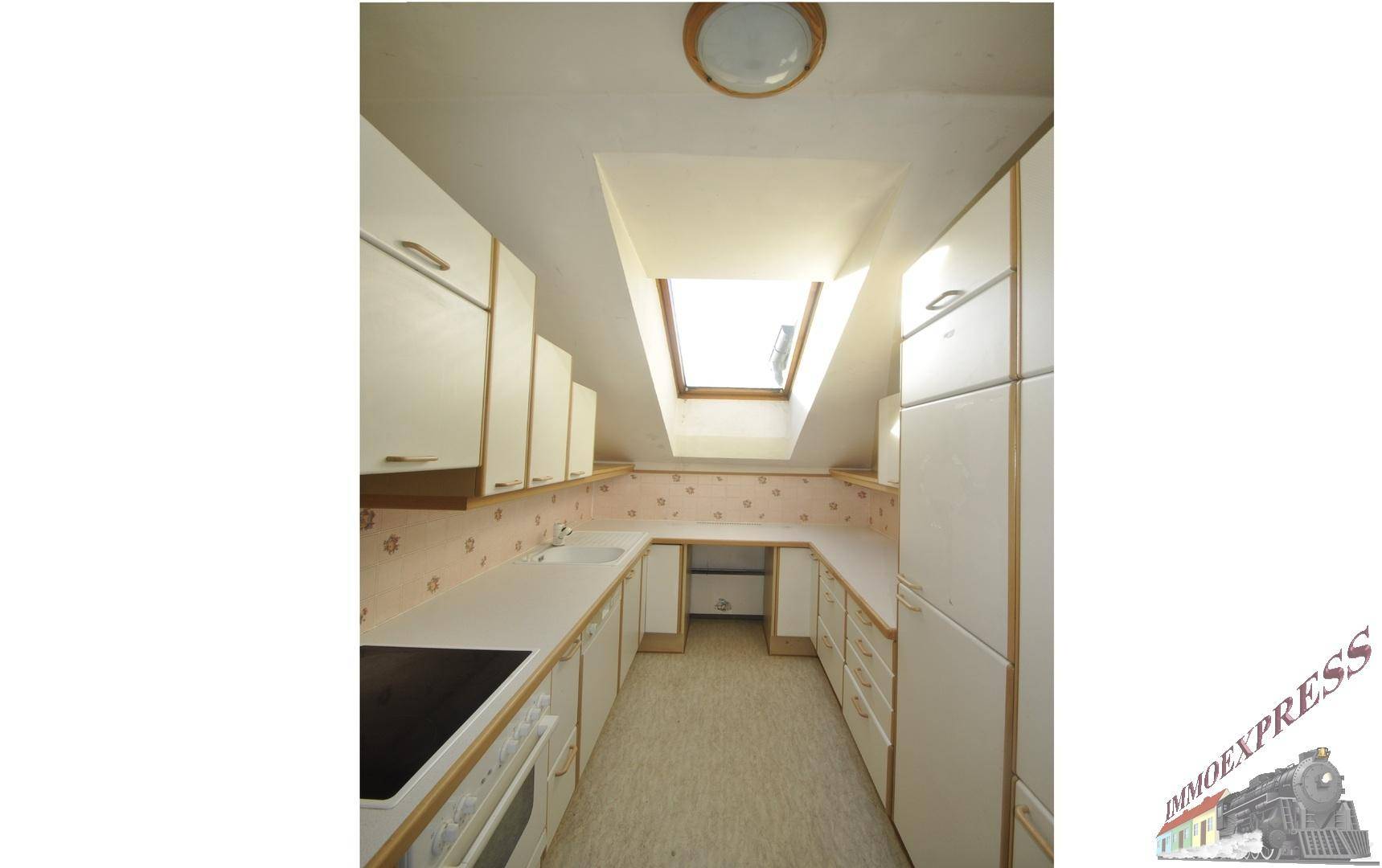 Küche im Dachgeschoss mit weißen Einbauschränken, Dachfenster und schräger Decke.