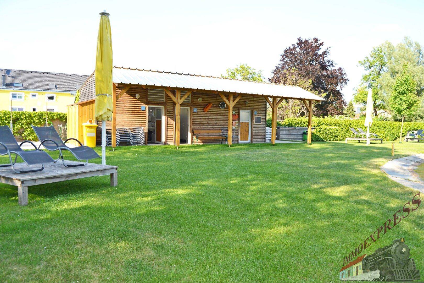 Gemeinschaftlicher Gartenbereich mit Holzgebäude, Liegestühlen und Sonnenschirm, lädt zum Entspannen ein.
