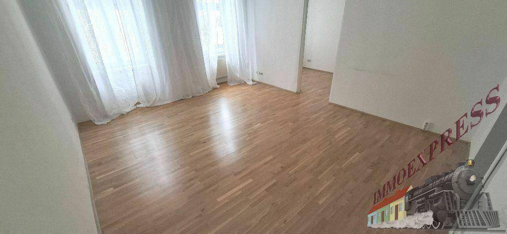 Geräumiges Wohnzimmer mit hellem Parkettboden, großen Fenstern und viel natürlichem Licht.