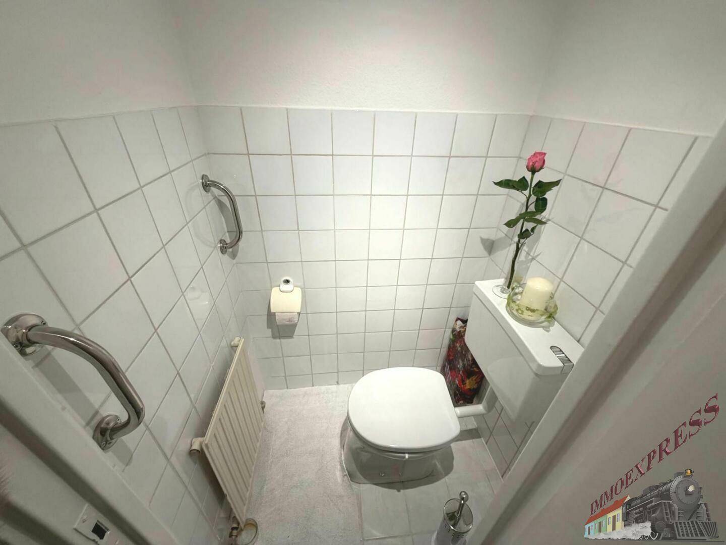 Kleines Gäste-WC mit weißen Fliesen, Toilette und Haltegriffen für Barrierefreiheit.