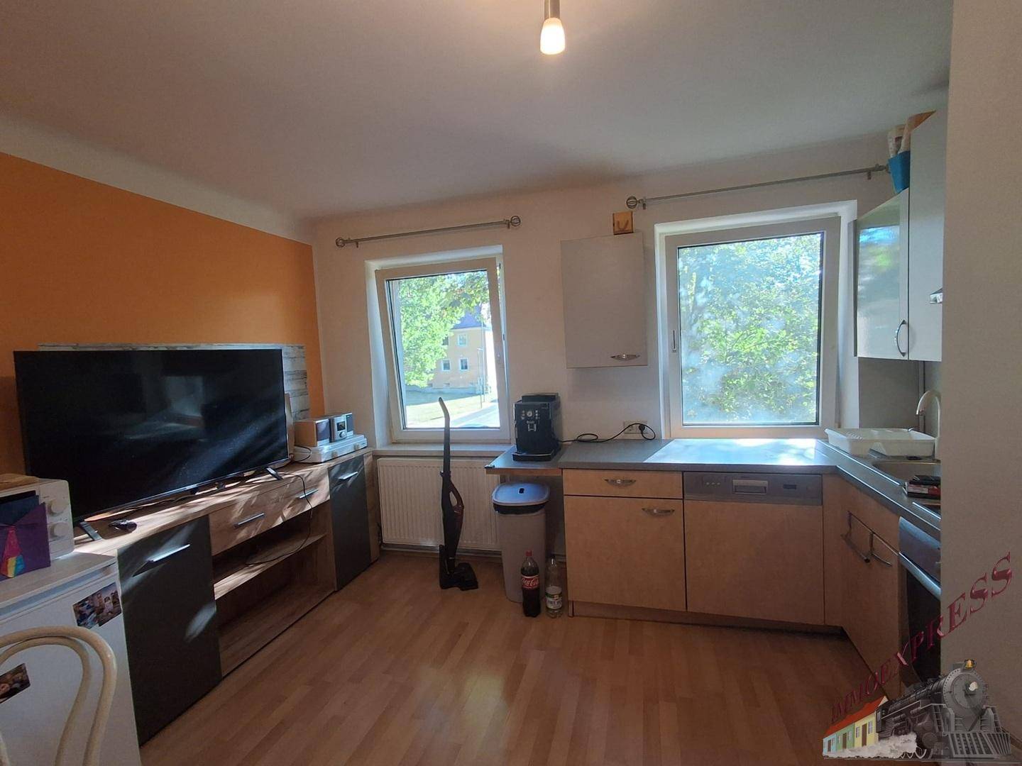Küche mit Einbauschränken, Arbeitsplatte, zwei Fenstern und orangefarbener Akzentwand.