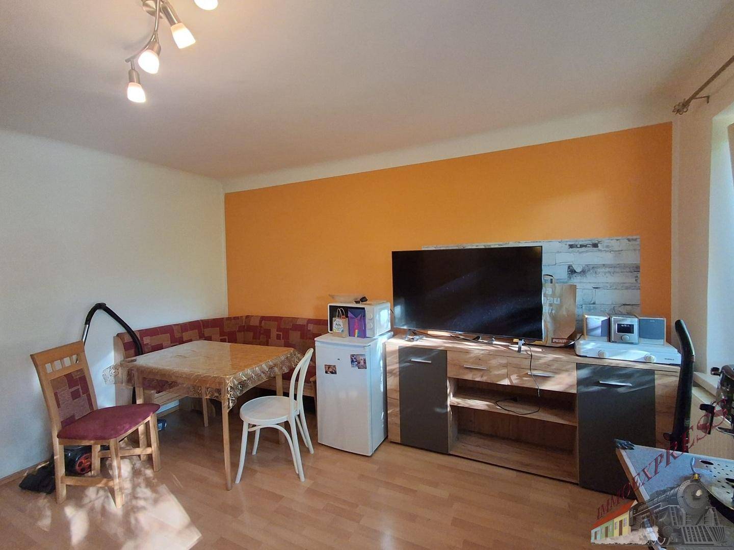 Gemütlicher Wohn-Essbereich mit Eckbank, Esstisch, Fernseher und orangefarbener Wand.
