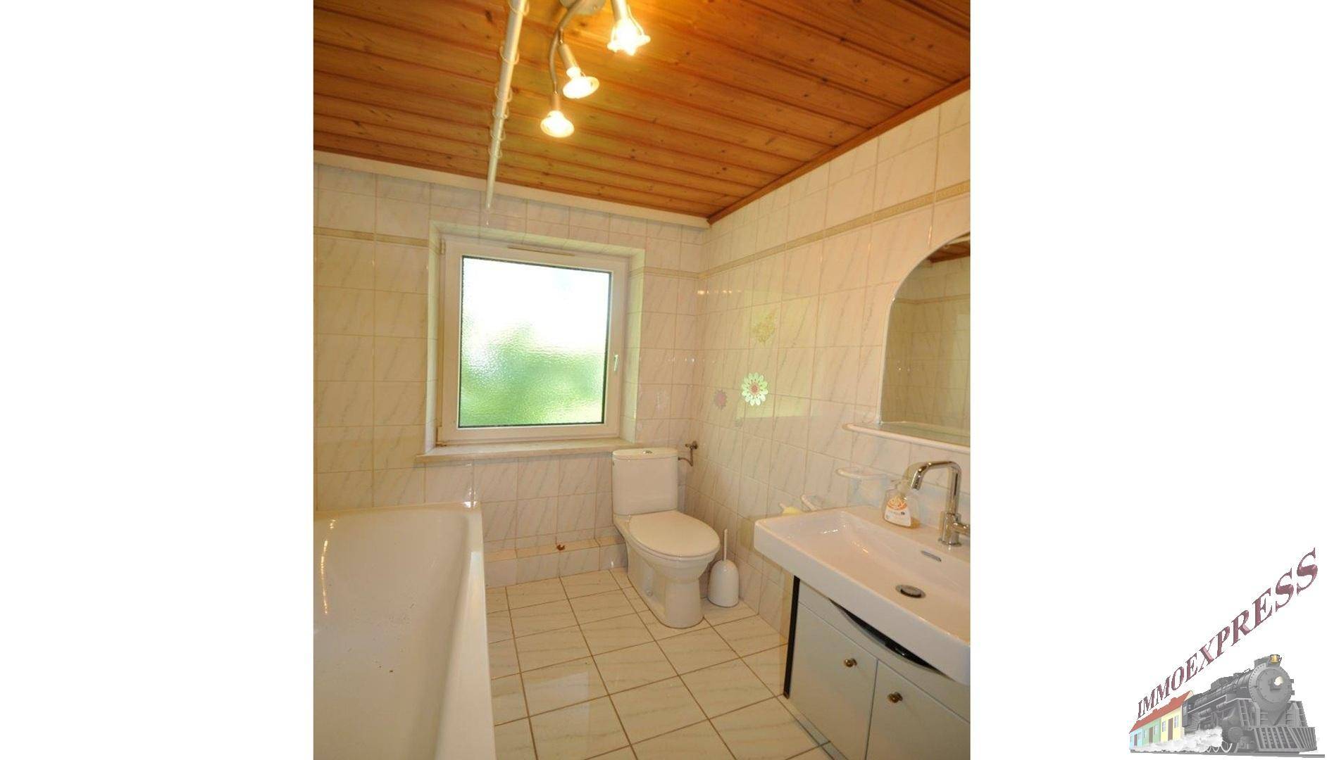 Badezimmer mit Badewanne, WC, Waschbecken, Fenster und Holzdecke.