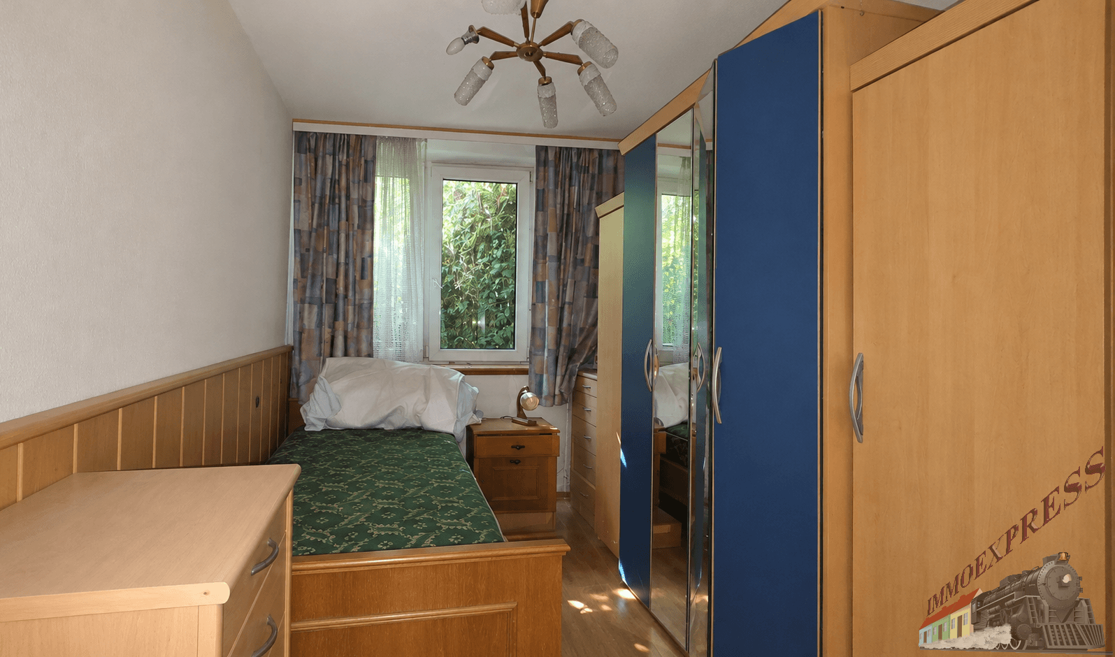Helles Schlafzimmer mit Einzelbett, Holzmöbeln und einem blauen Kleiderschrank.