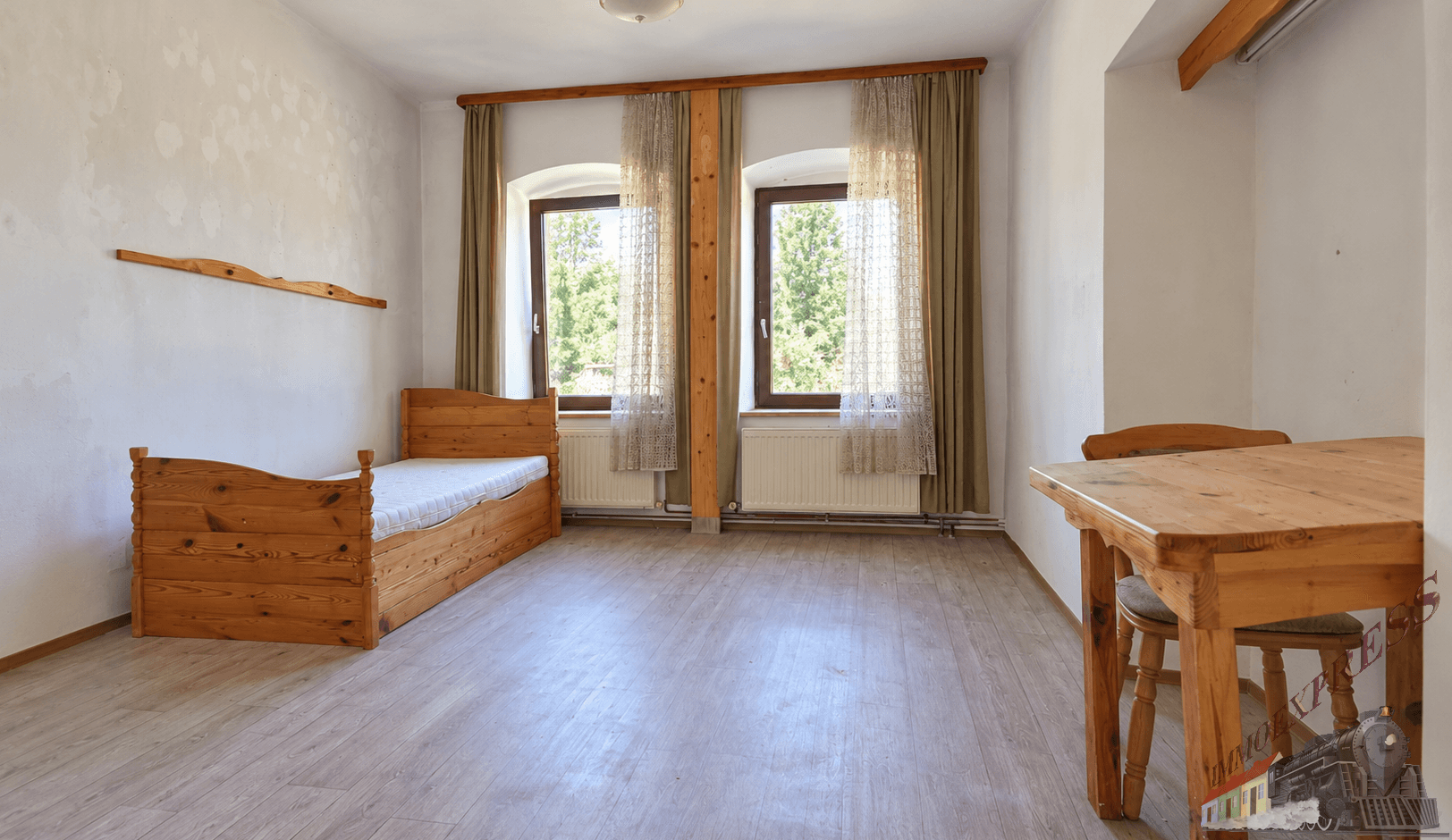 Helles Schlafzimmer mit Laminatboden, zwei Fenstern und einfacher Holzmöblierung.