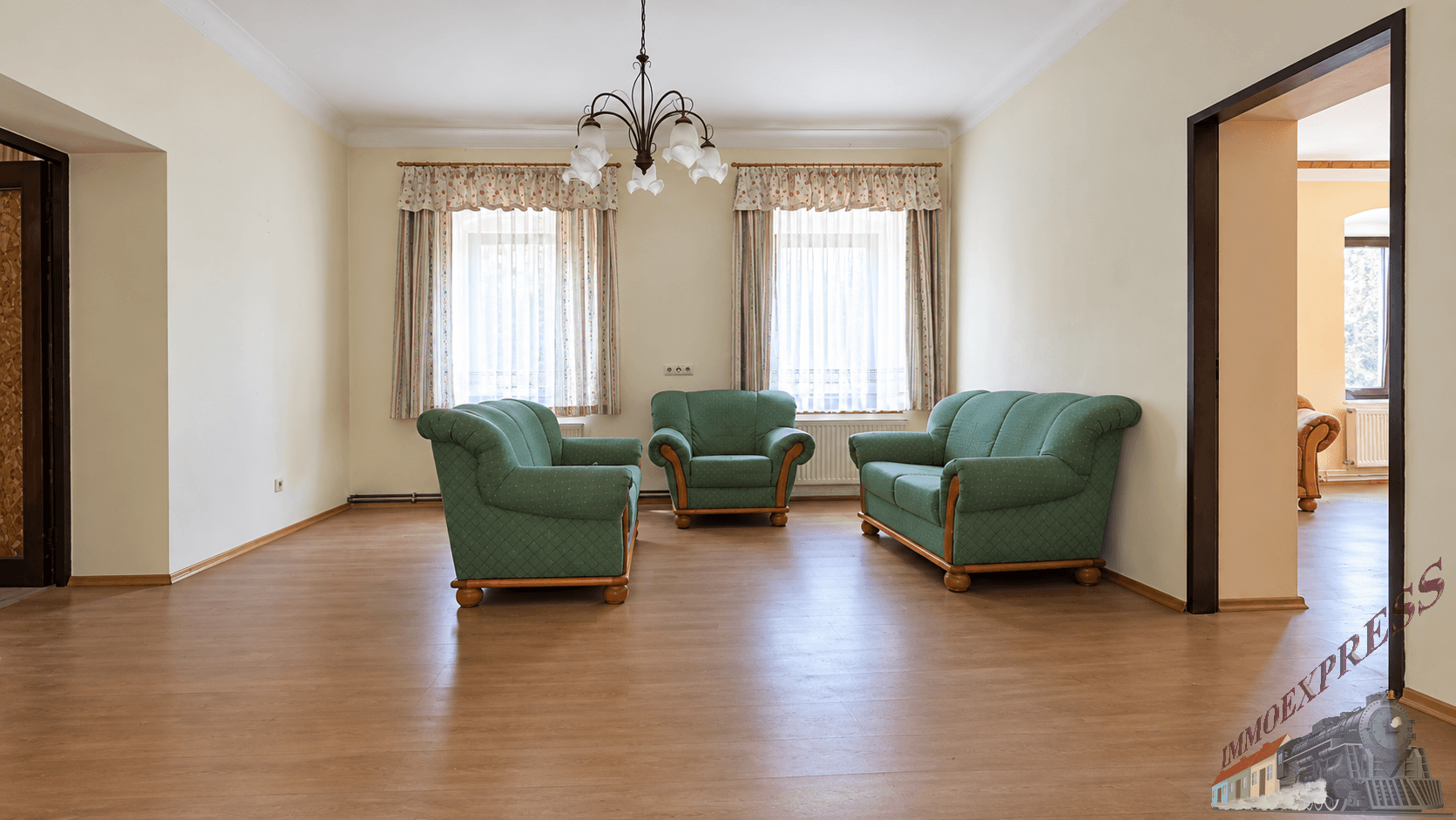 Helles Wohnzimmer mit Laminatboden, drei grünen Sofas und einem klassischen Kronleuchter.
