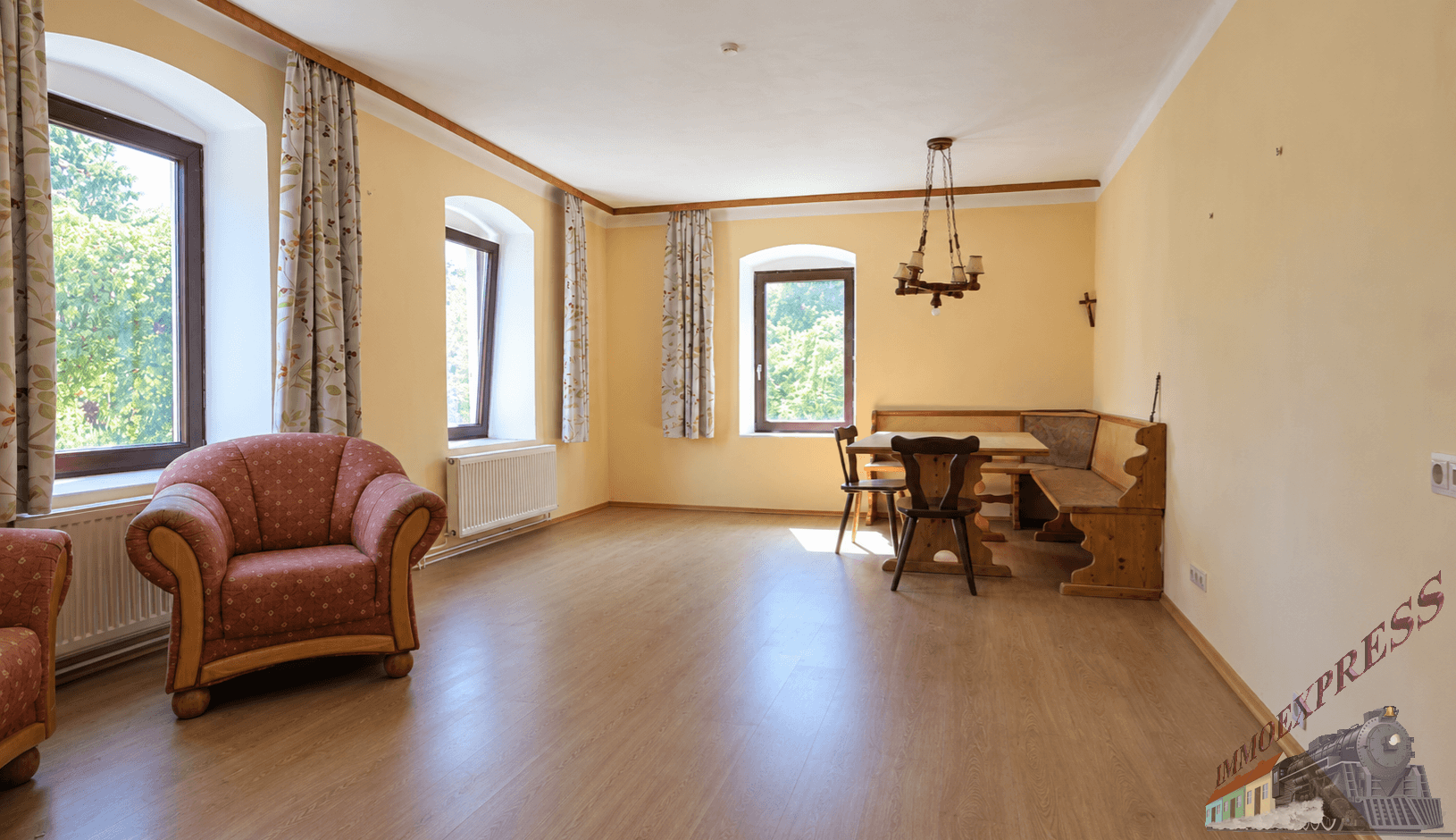 Wohn-Essbereich mit Laminatboden, rotem Sessel und traditioneller Holzeckbank am Esstisch.
