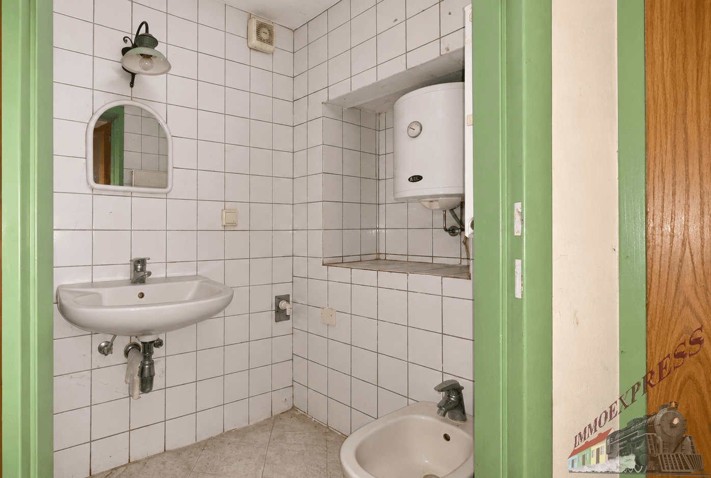 Gefliestes Badezimmer mit Waschbecken, Bidet und einem Warmwasserboiler an der Wand.