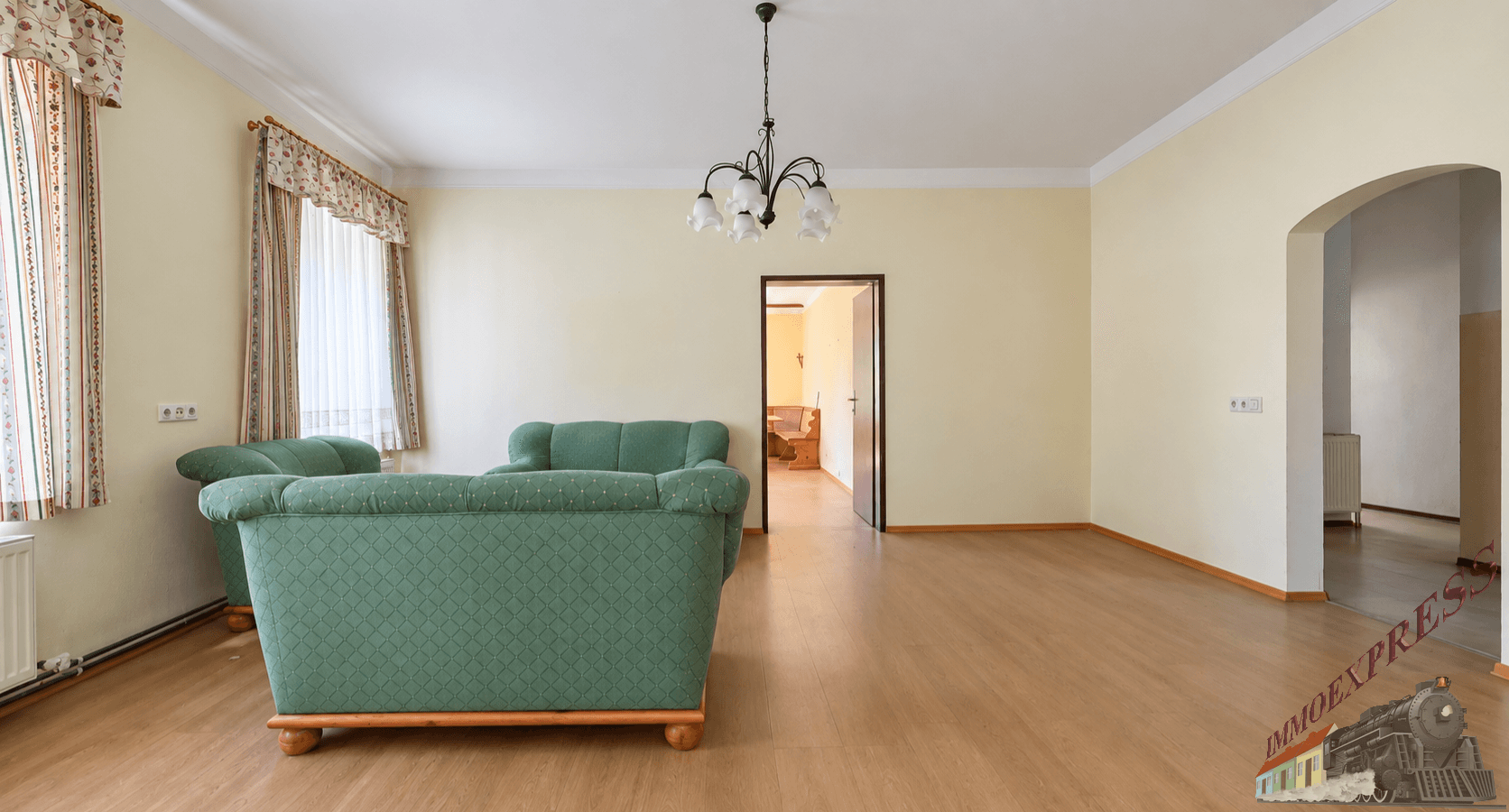 Geräumiges Wohnzimmer mit Laminatboden, zwei grünen Sofas und einem Kronleuchter.