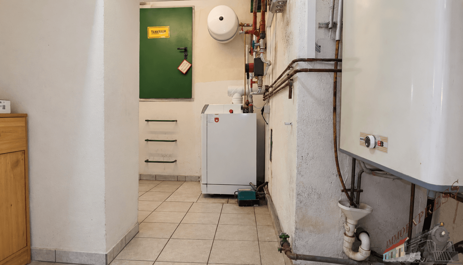 Heizungsraum mit Boiler, sichtbaren Rohren und Fliesenboden, funktional und gut erhalten.