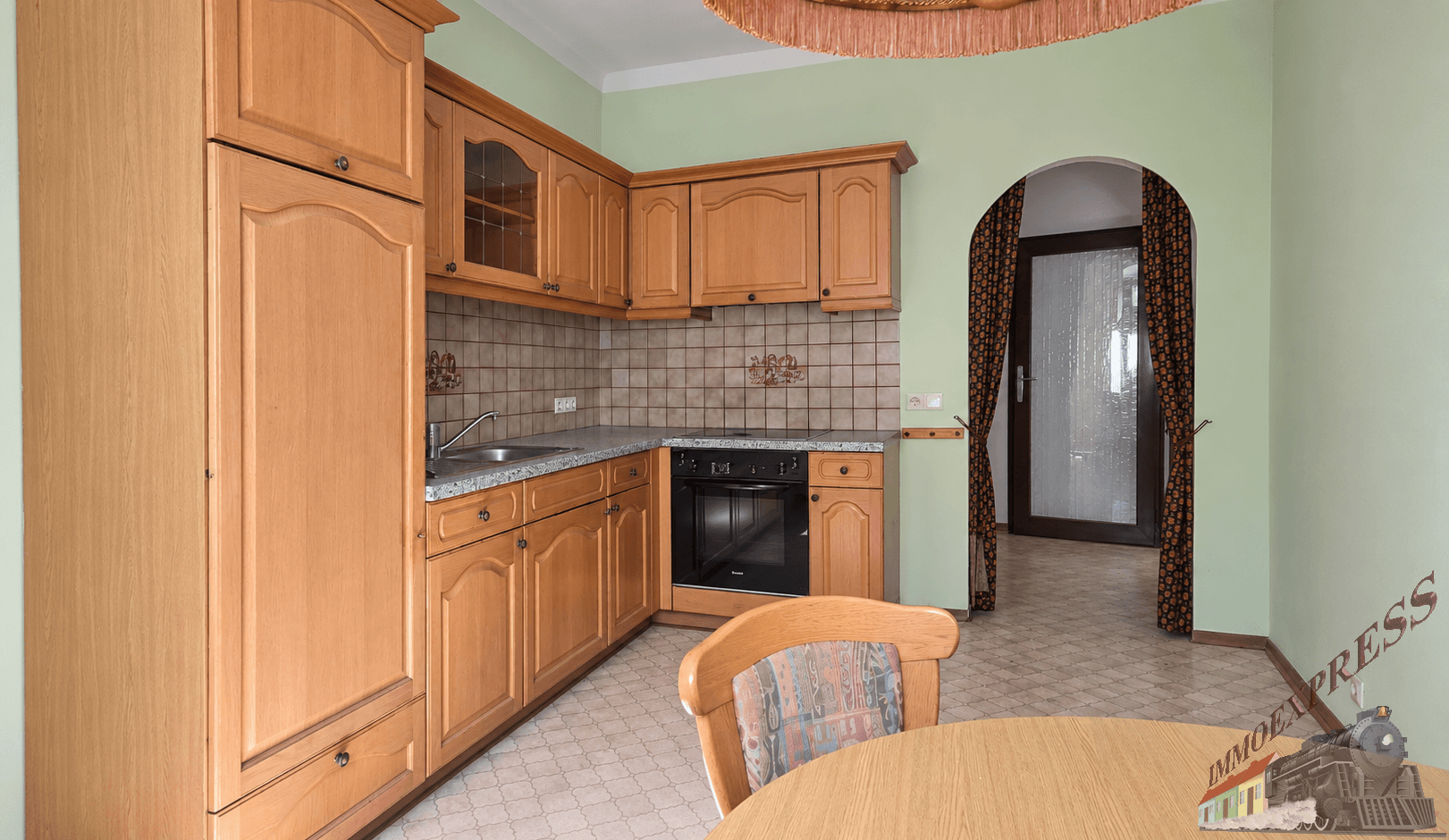 Funktionale Küche mit Holzschränken, eingebautem Backofen und Kochfeld, sowie einem Rundbogen.