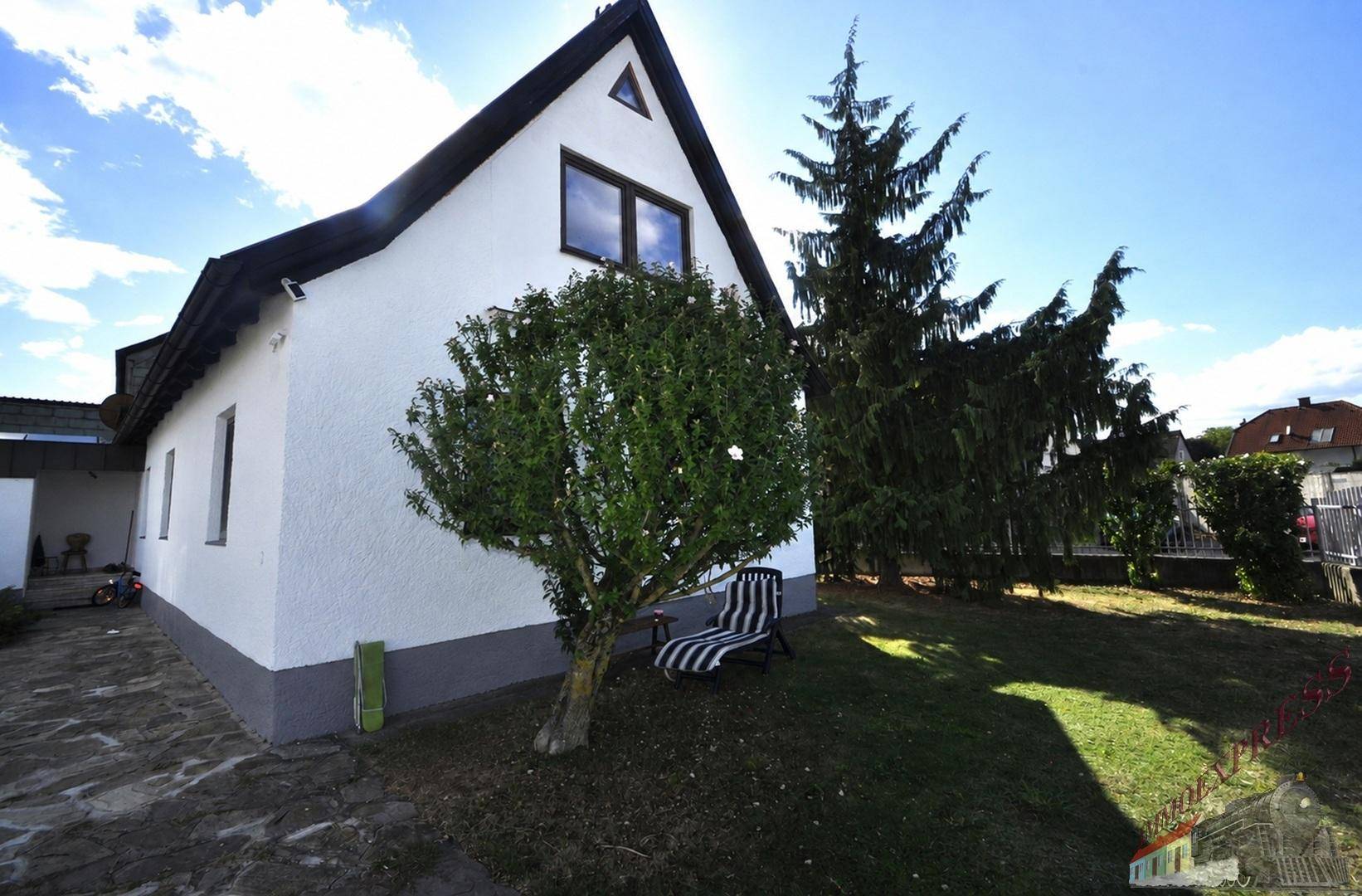 Seitenansicht des Einfamilienhauses mit gepflegtem Rasen und hohen Bäumen unter strahlendem Himmel.