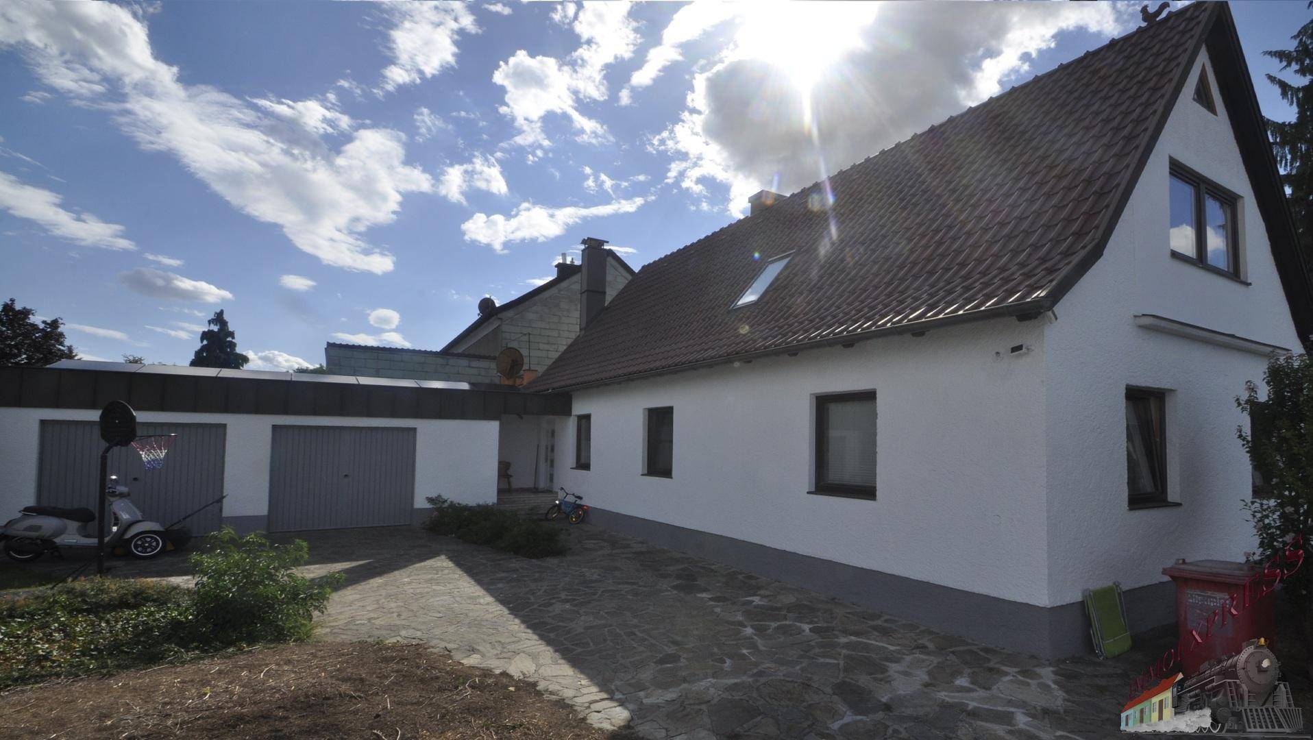 Ansicht des Einfamilienhauses mit angrenzender Garage und gepflasterter Zufahrt bei Sonnenschein.
