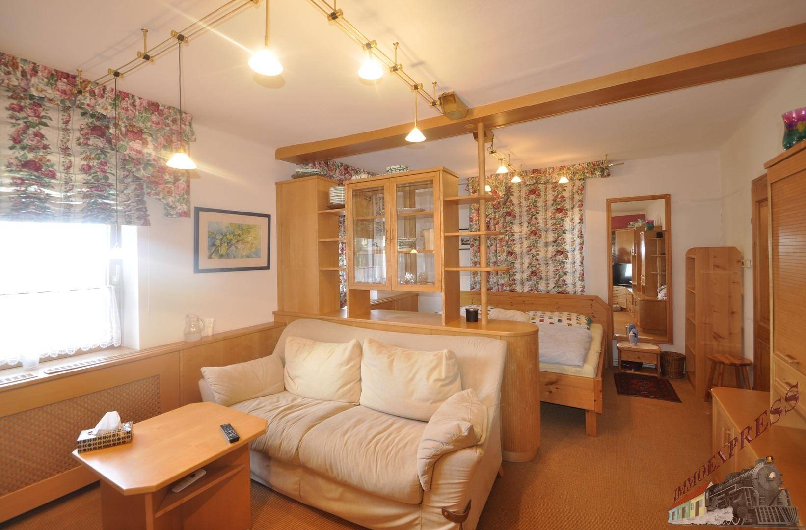 Gemütliches Schlafzimmer mit Sofa, Holzmöbeln und floralen Vorhängen, ideal zum Entspannen.