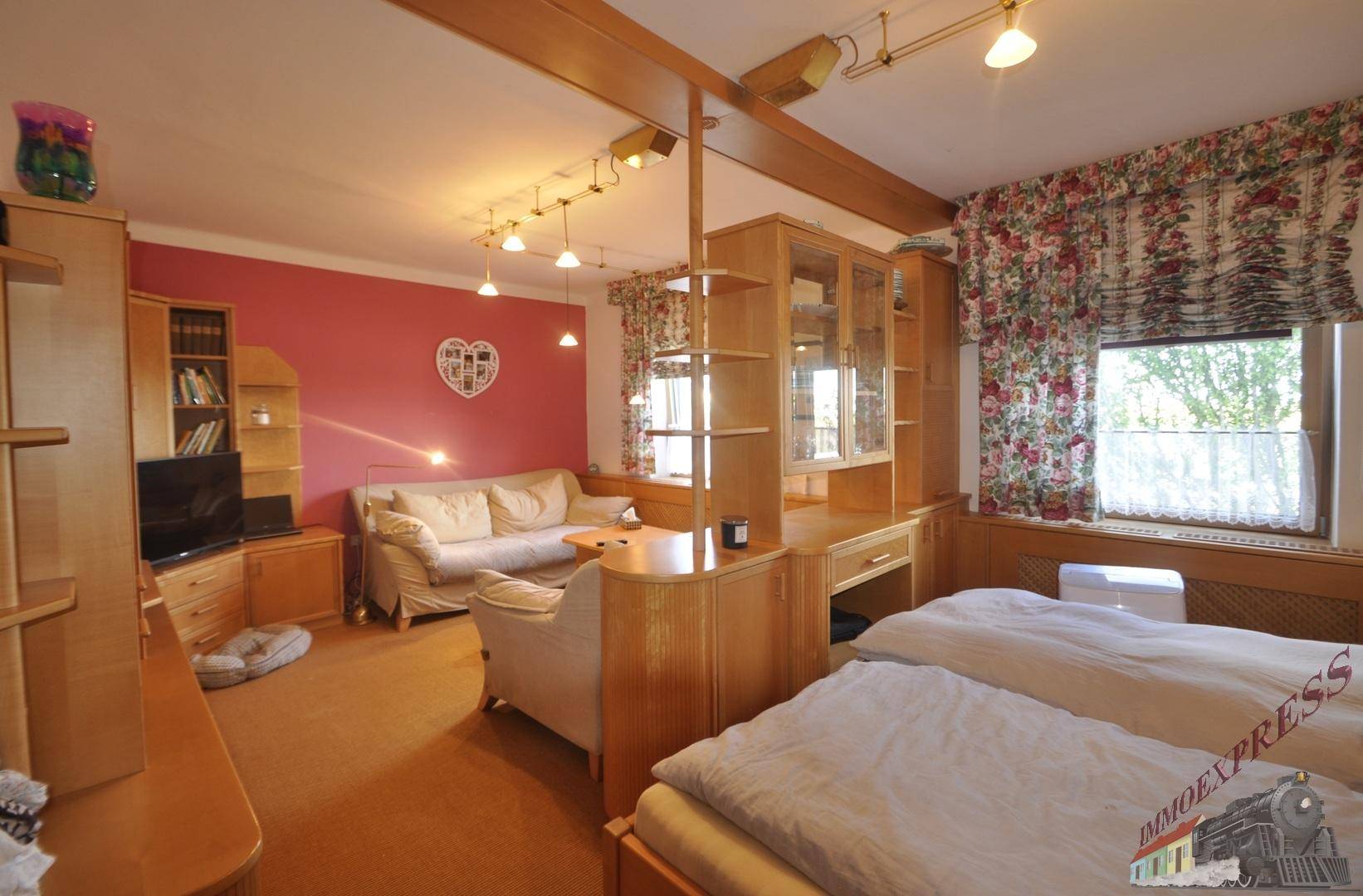Helles Schlafzimmer mit Doppelbett, Holzmöbeln und rosa Wandakzenten, mit Blick nach draußen.