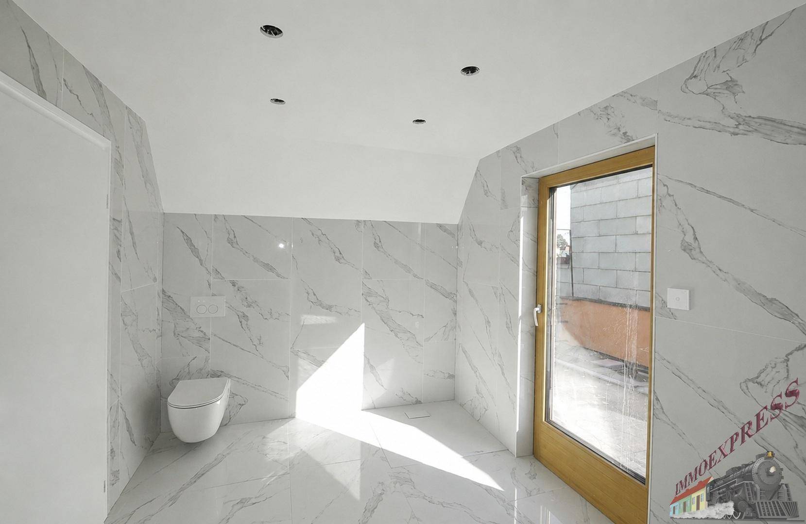 Geräumiges Badezimmer im Rohbau mit Marmorfliesen, wandhängender Toilette und viel Tageslicht.