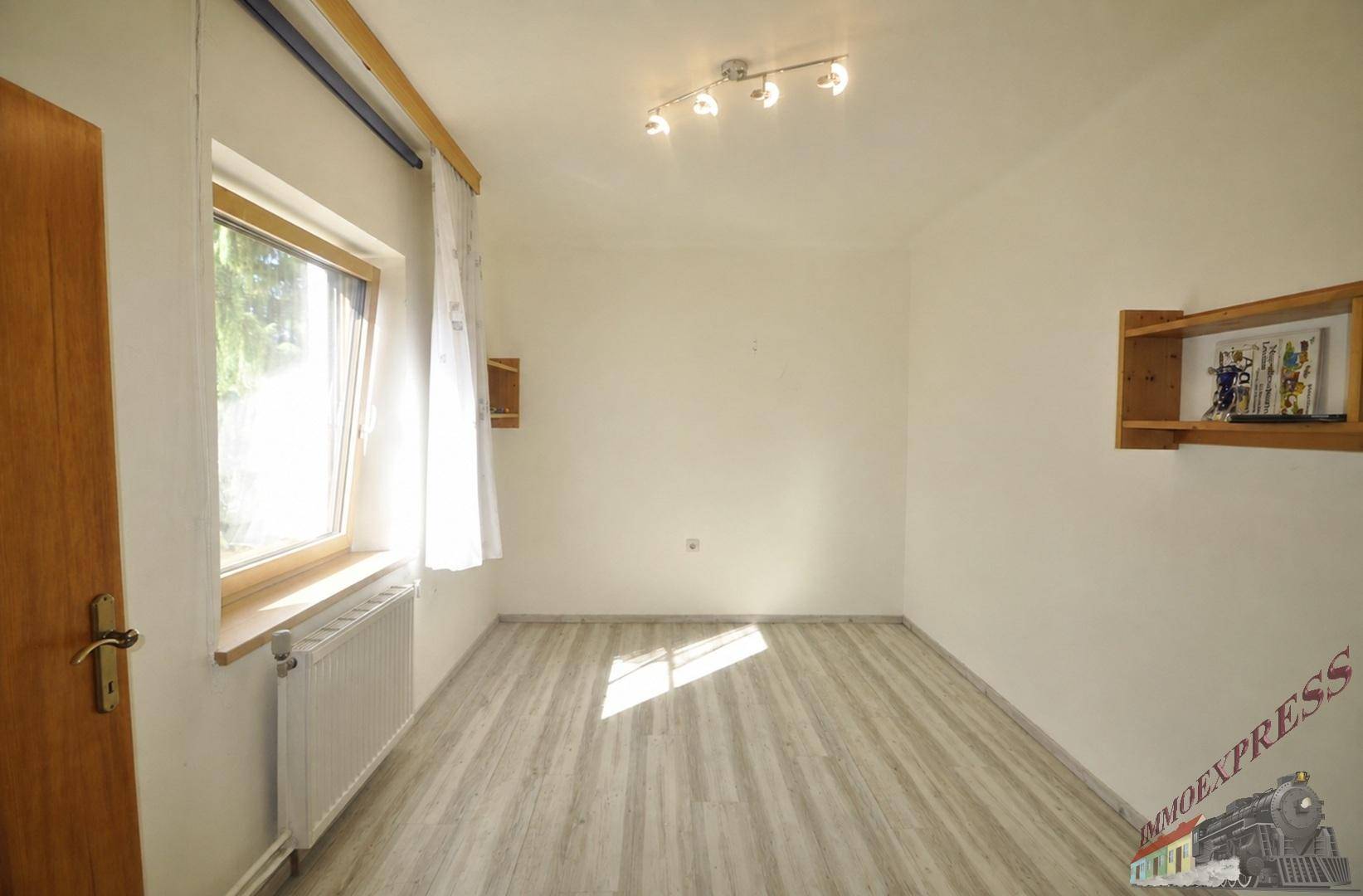Helles Zimmer mit Laminatboden, weiß gestrichenen Wänden und einem großen Fenster.