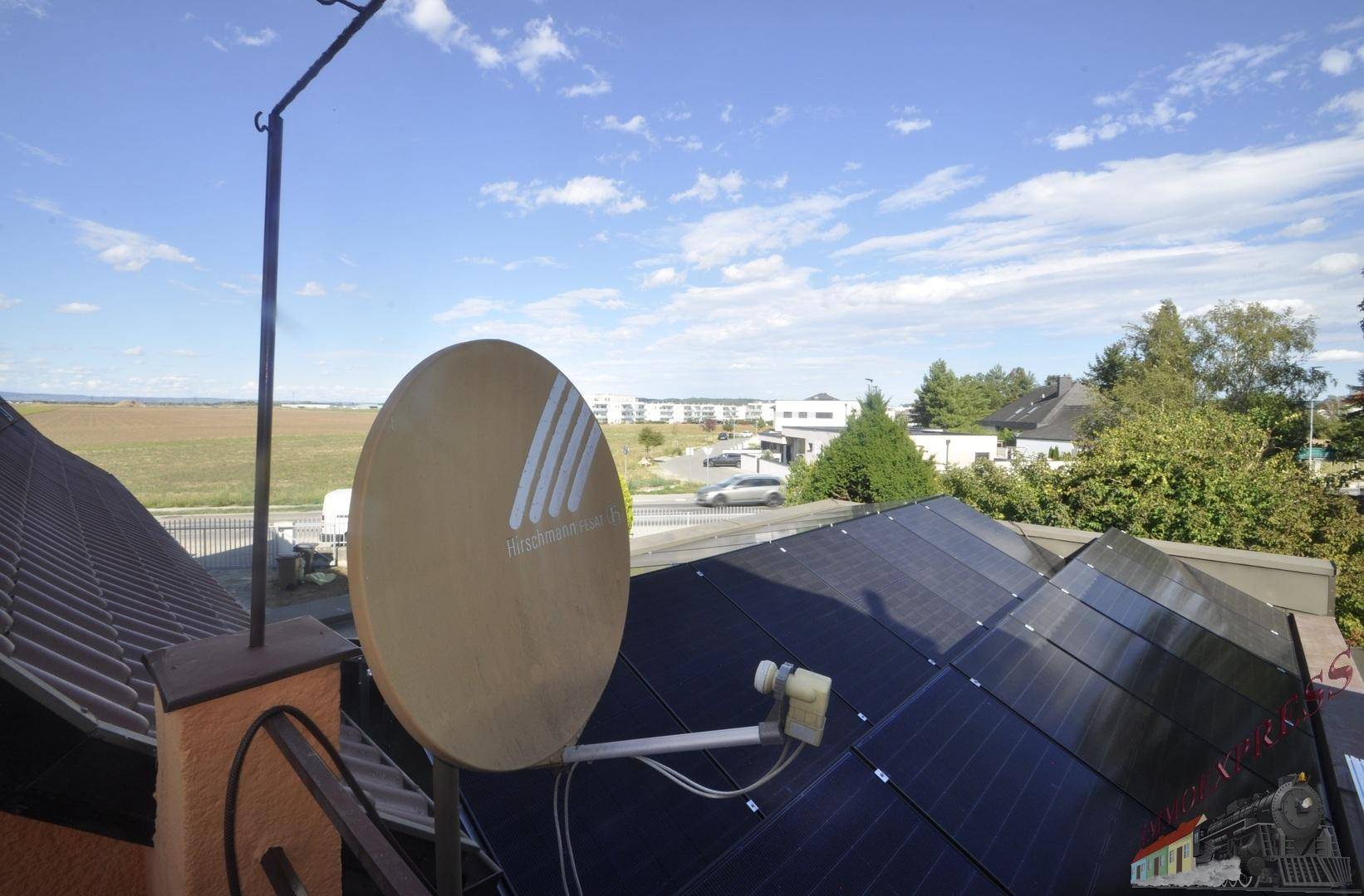 Dachansicht mit Photovoltaikanlage und Satellitenschüssel, umgeben von ländlicher Landschaft.