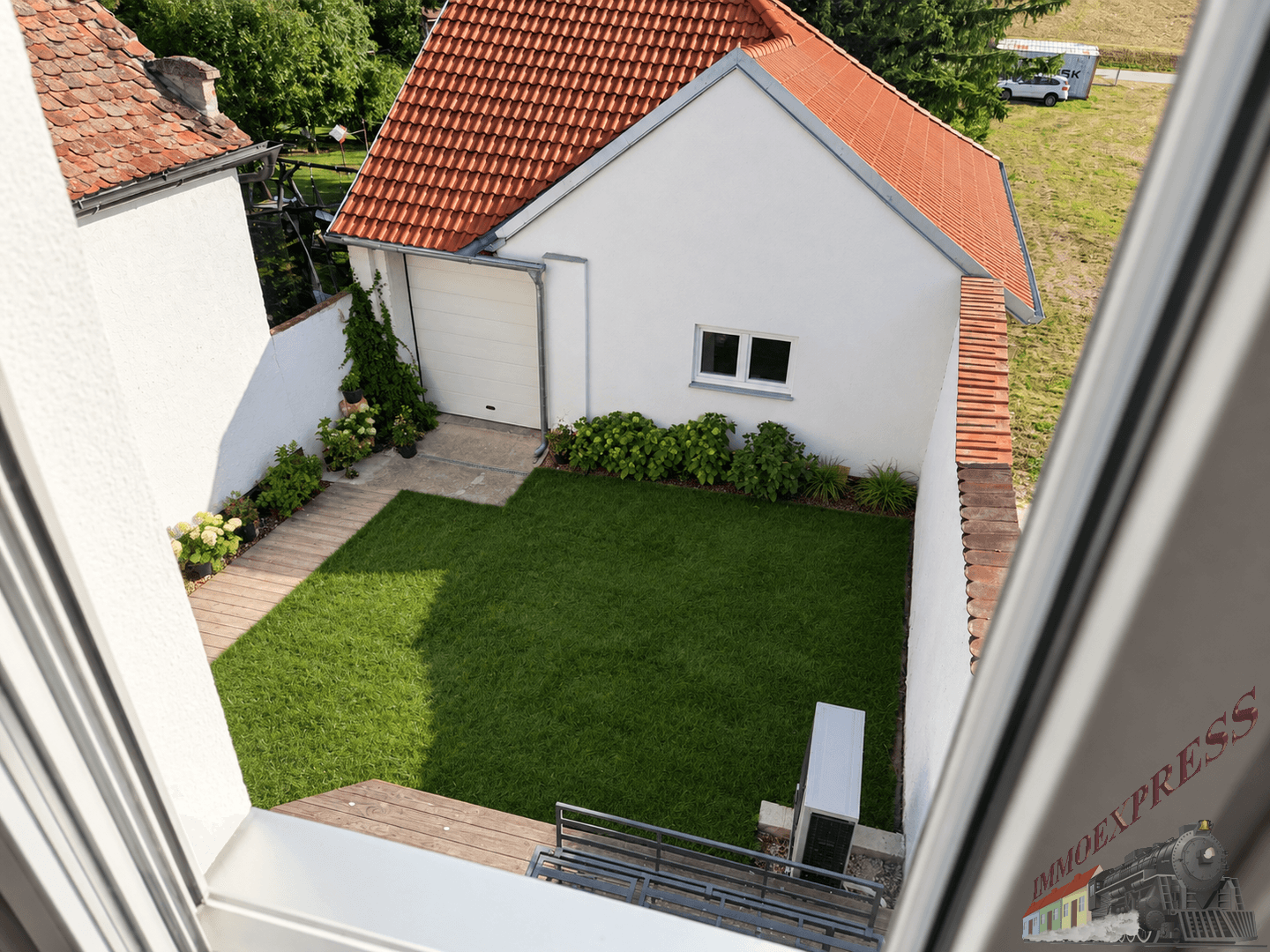 Blick von oben auf den gepflegten Gartenbereich mit Rasen, Terrasse und Nebengebäude.