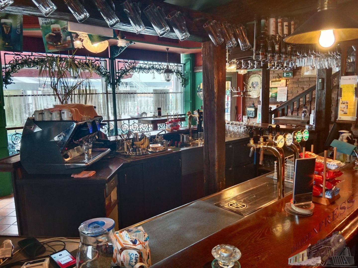 Geräumige Bar mit Holztheke, Zapfanlagen und Blick durch große Fenster nach draußen.