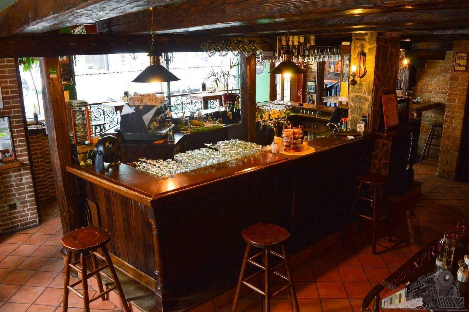 Ansicht der Holzbar mit Hockern und traditionellem Fliesenboden, beleuchtet von Hängelampen.