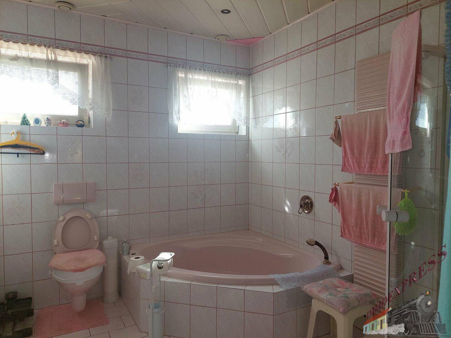 Badezimmer im 80er-Jahre-Stil mit rosa Eckbadewanne, WC und weißen Fliesen.