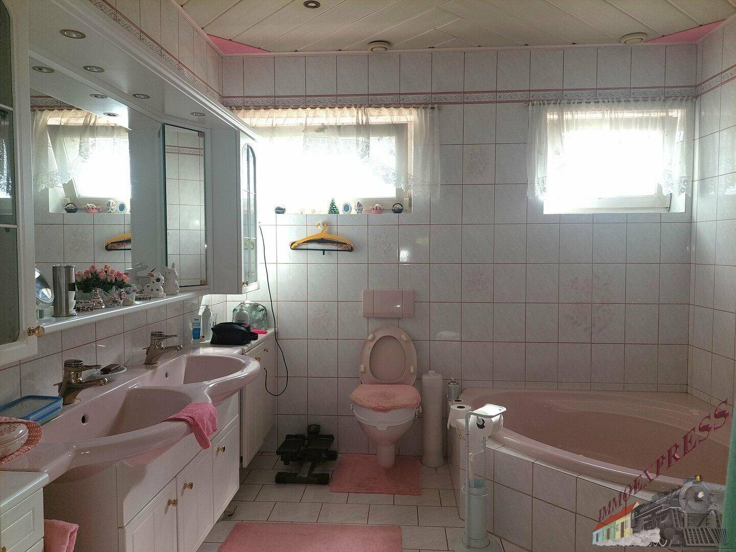 Geräumiges Badezimmer mit Doppelwaschbecken, rosa Badewanne und weißen Fliesen.
