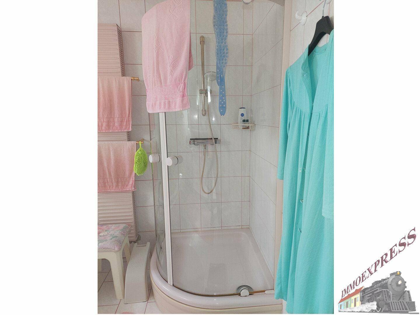 Duschkabine im Badezimmer mit weißen Fliesen und Handtuchhalter.