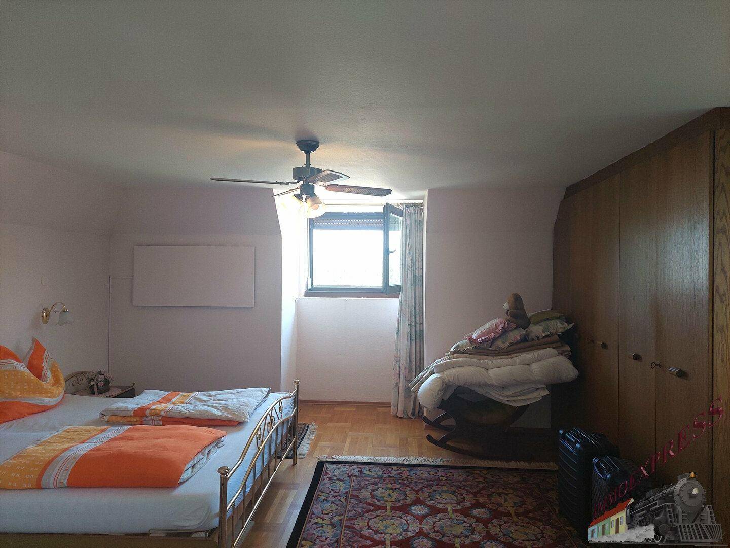 Schlafzimmer im Dachgeschoss mit Holzboden, Deckenventilator und Dachschräge.