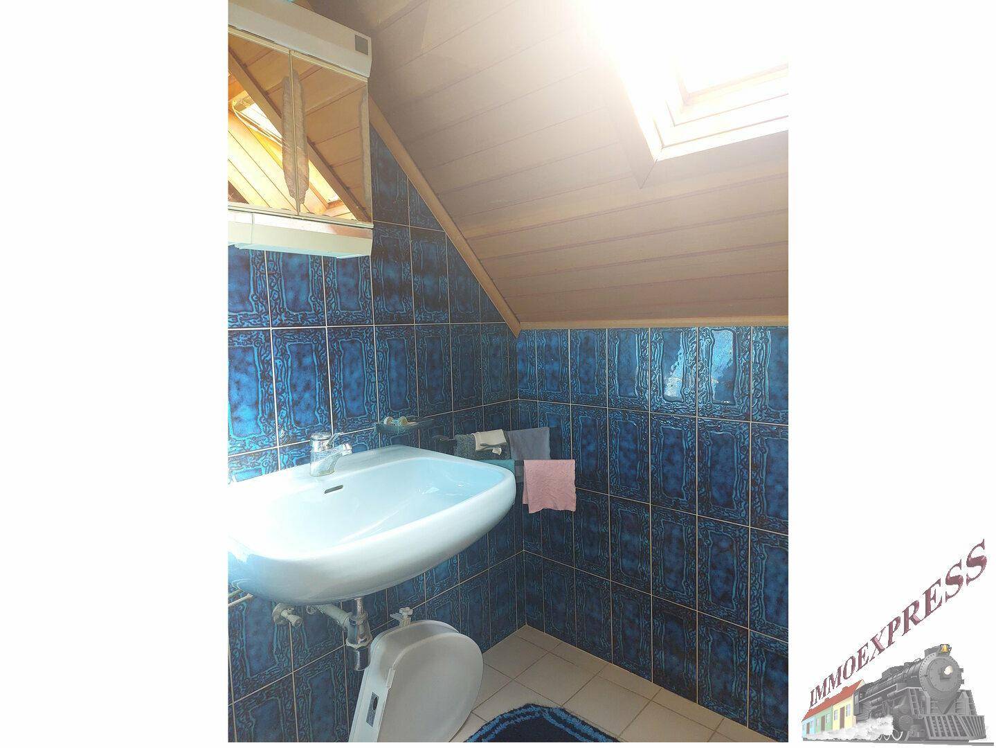 Kleines WC im Dachgeschoss mit blauen Fliesen, Waschbecken und Dachfenster.
