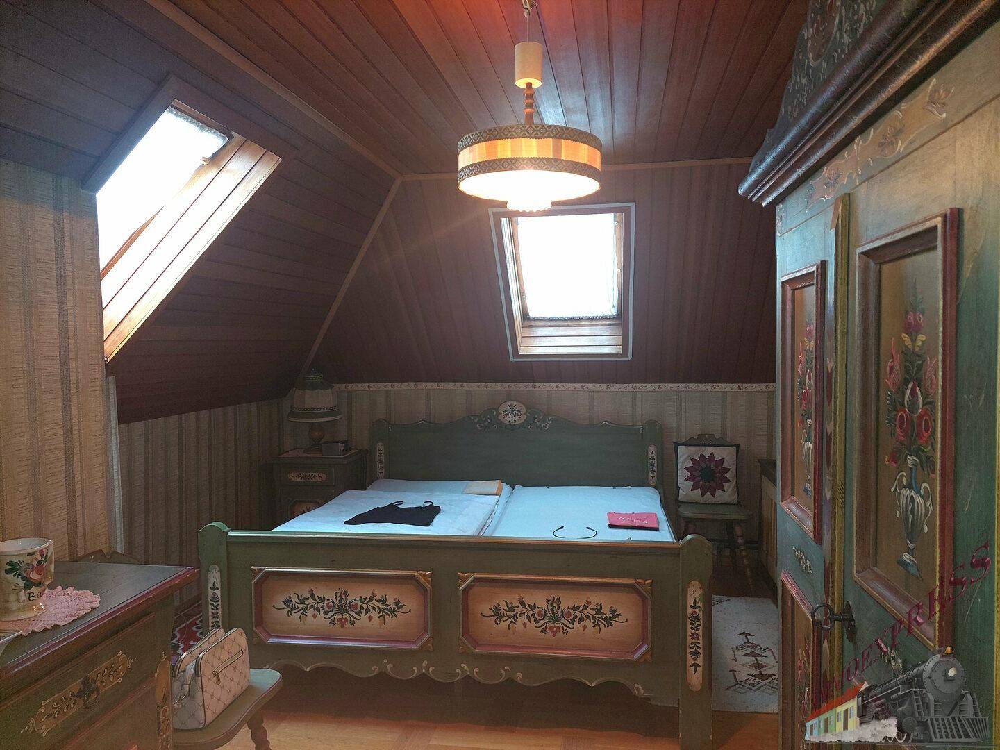 Rustikales Schlafzimmer im Dachgeschoss mit bemalten Möbeln und Holzverkleidung.