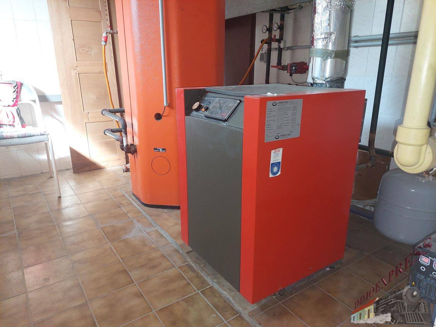 Heizungsanlage mit großem Warmwasserspeicher in einem gefliesten Raum im Keller.