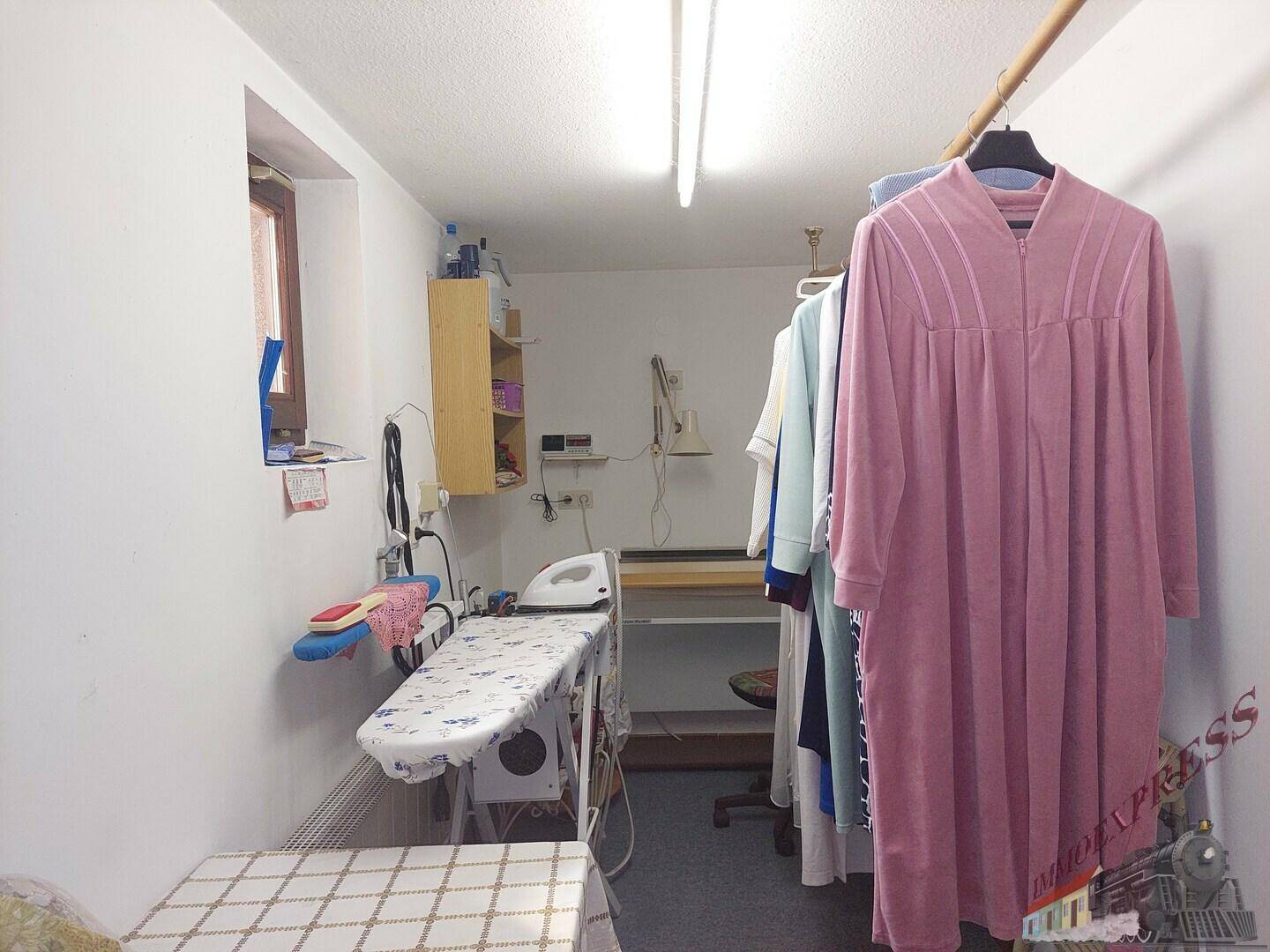 Bügelzimmer im Untergeschoss mit Bügelbrett, Regalen und Fenster.