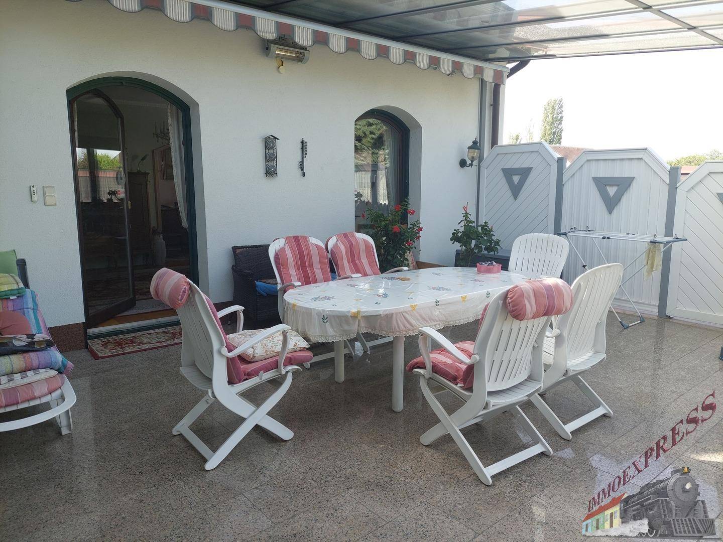 Gemütliche überdachte Terrasse mit Esstisch und Stühlen, ideal für Mahlzeiten im Freien.