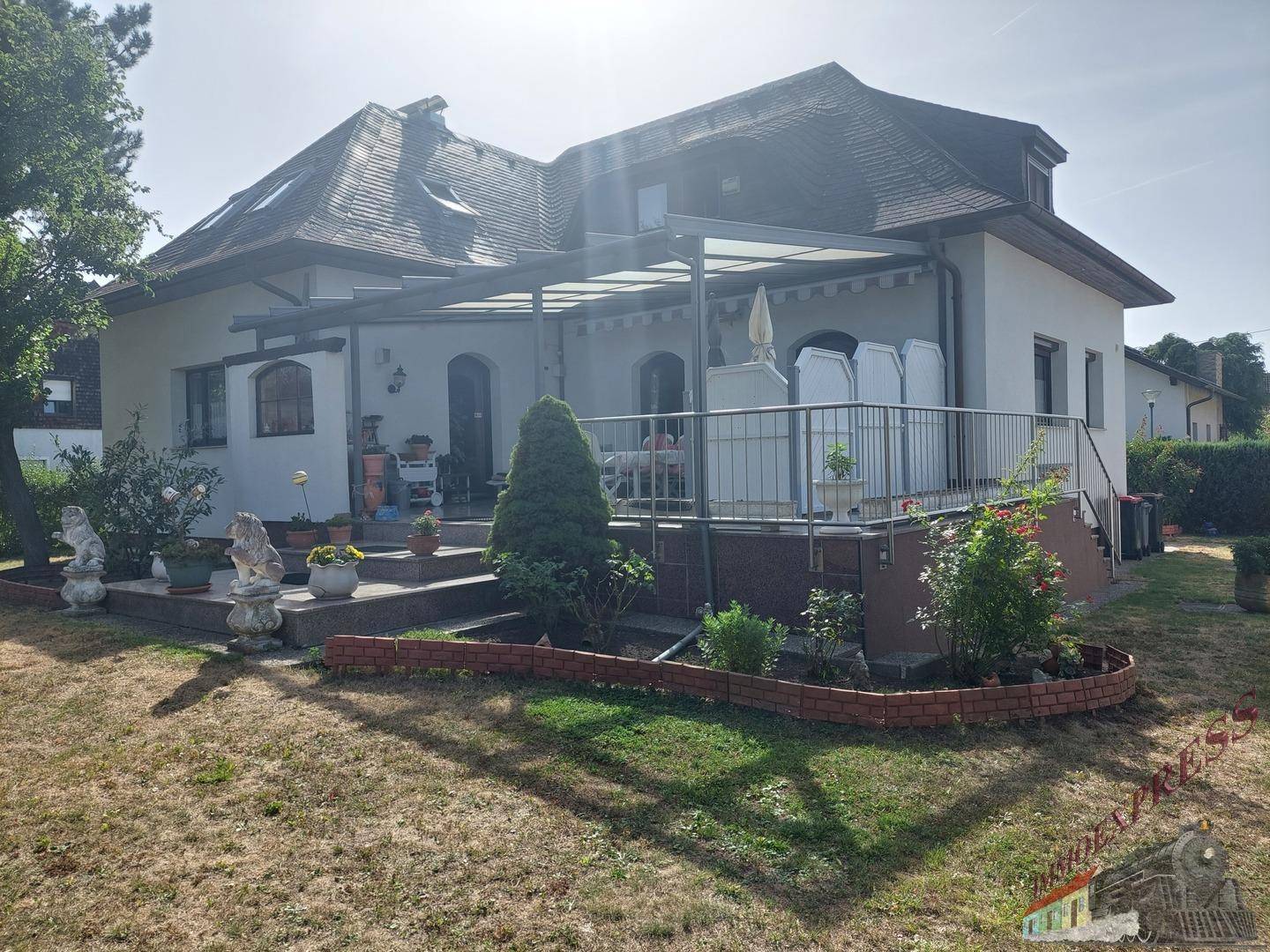 Charmantes Haus mit überdachter Terrasse und weitläufigem Garten an einem sonnigen Tag.