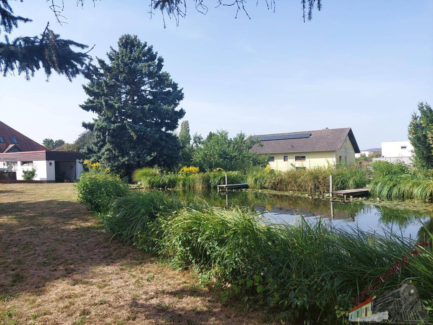 Weitläufiger Gartenbereich mit Teich und Blick auf ein weiteres Gebäude in der Ferne.