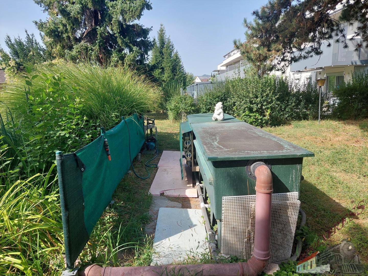 Gartenbereich mit technischer Ausstattung für den Teich und üppiger Bepflanzung.