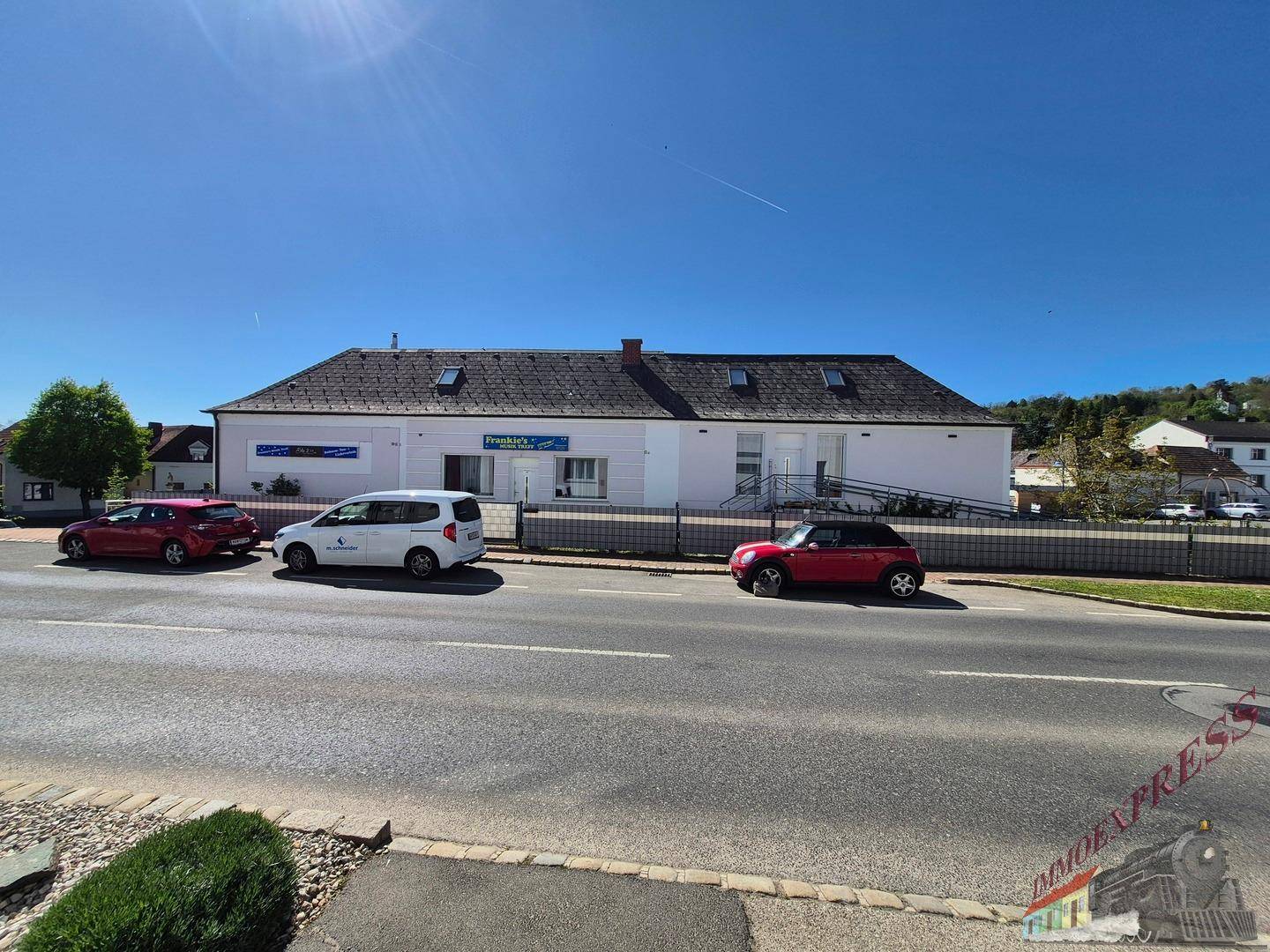 Gebäudeansicht von der Straße mit geparkten Autos und Rampe zum Eingang.