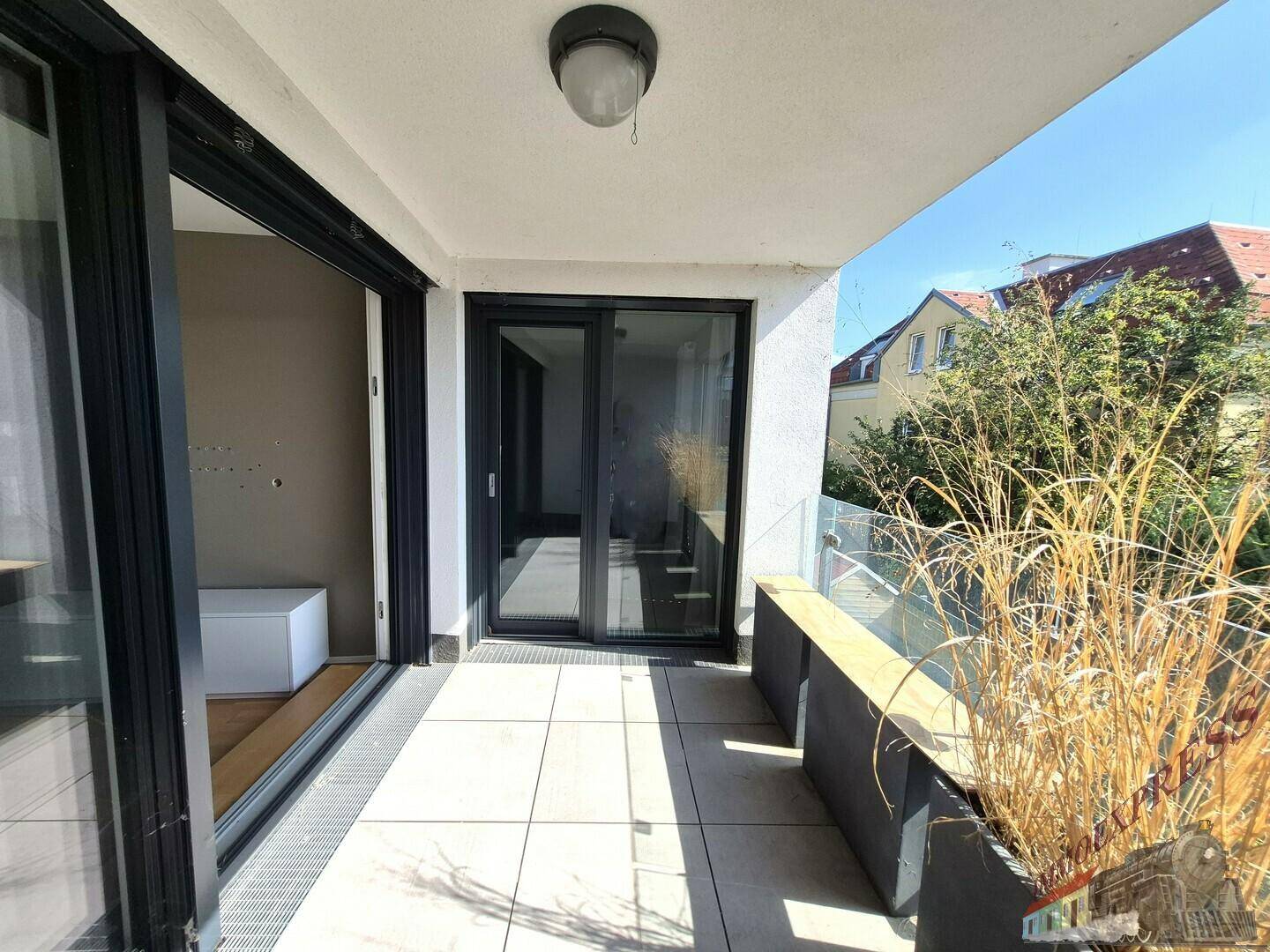 Heller Balkon mit Fliesenboden, Glasgeländer und Pflanzen, zugänglich vom Innenbereich.
