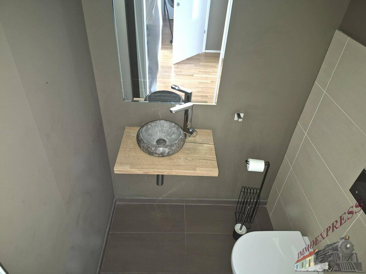 Gäste-WC mit modernem Steinwaschbecken, Wand-WC und dunklen Fliesen.