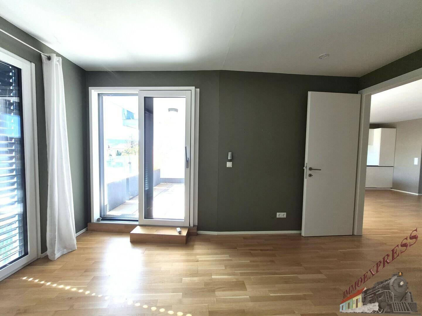 Geräumiger Raum mit Holzparkettboden und Zugang zu einem Außenbereich durch eine Schiebetür.